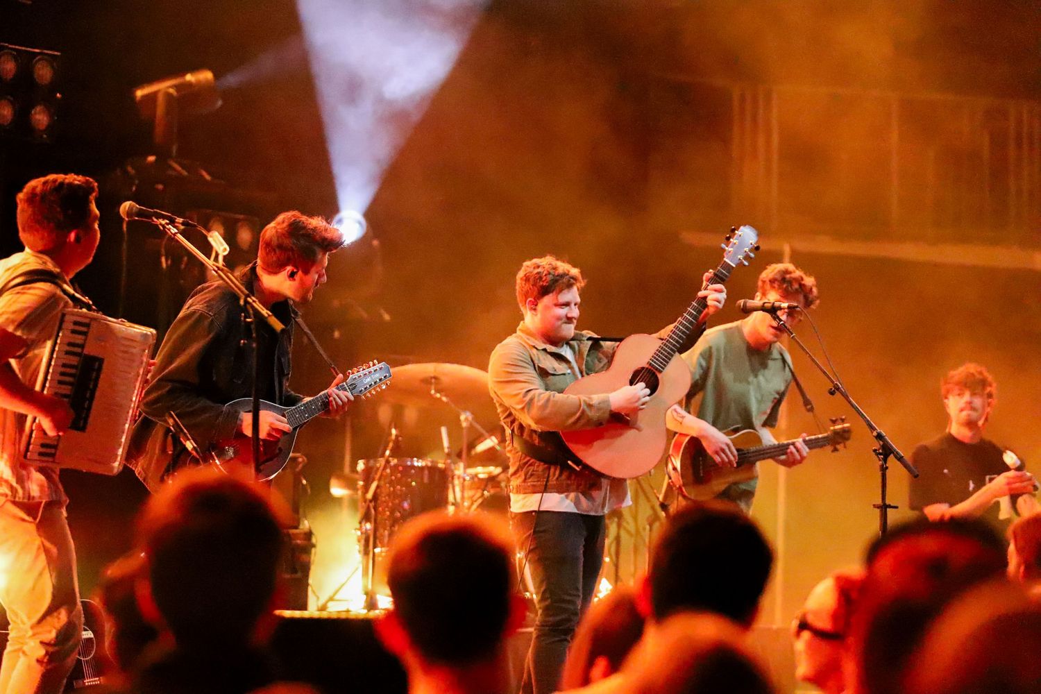 Band of four musicians performing on stage with warm orange lighting and an engaged crowd at a live show.