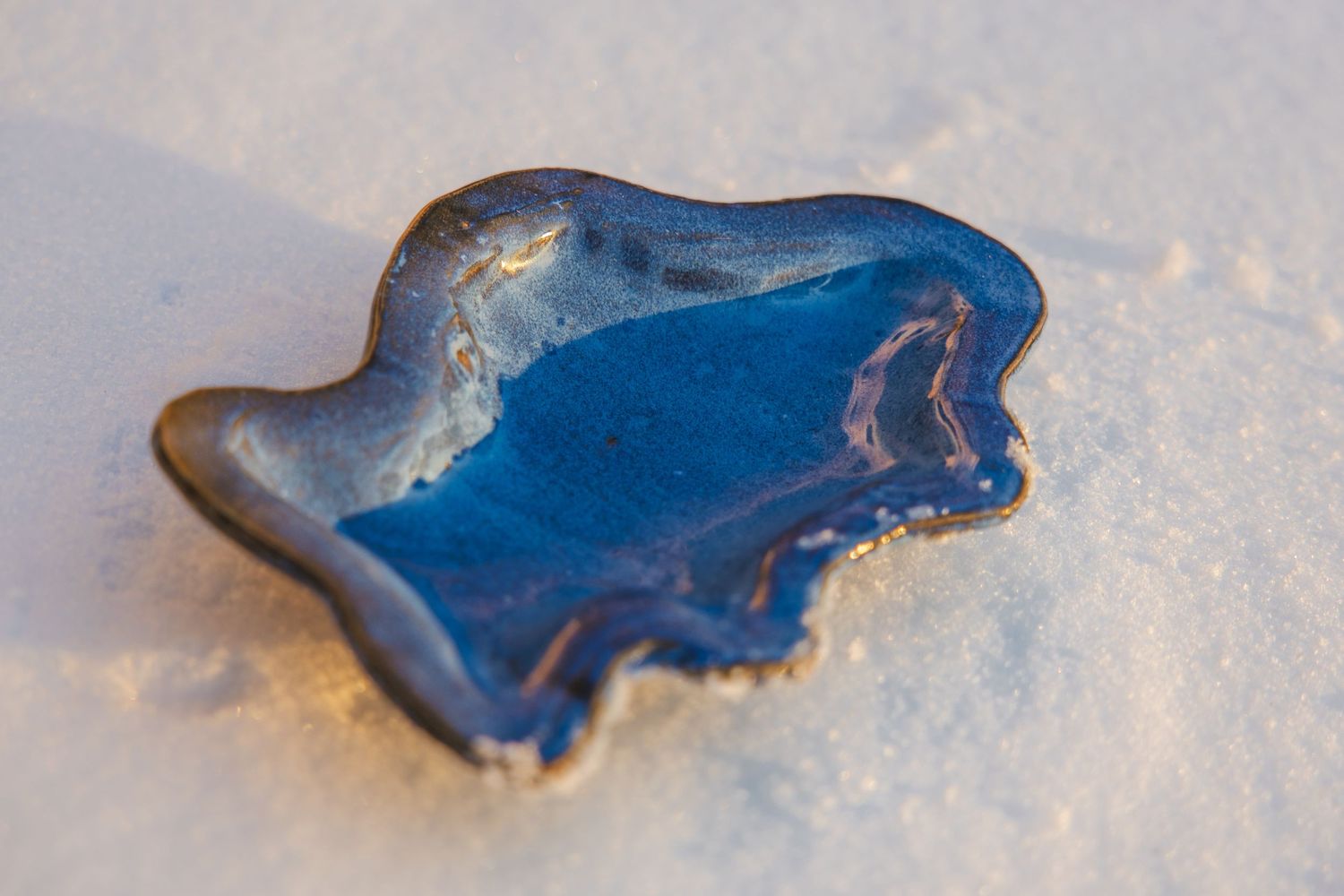 Blue glazed ceramic frog-shaped dish resting on white snow surface.