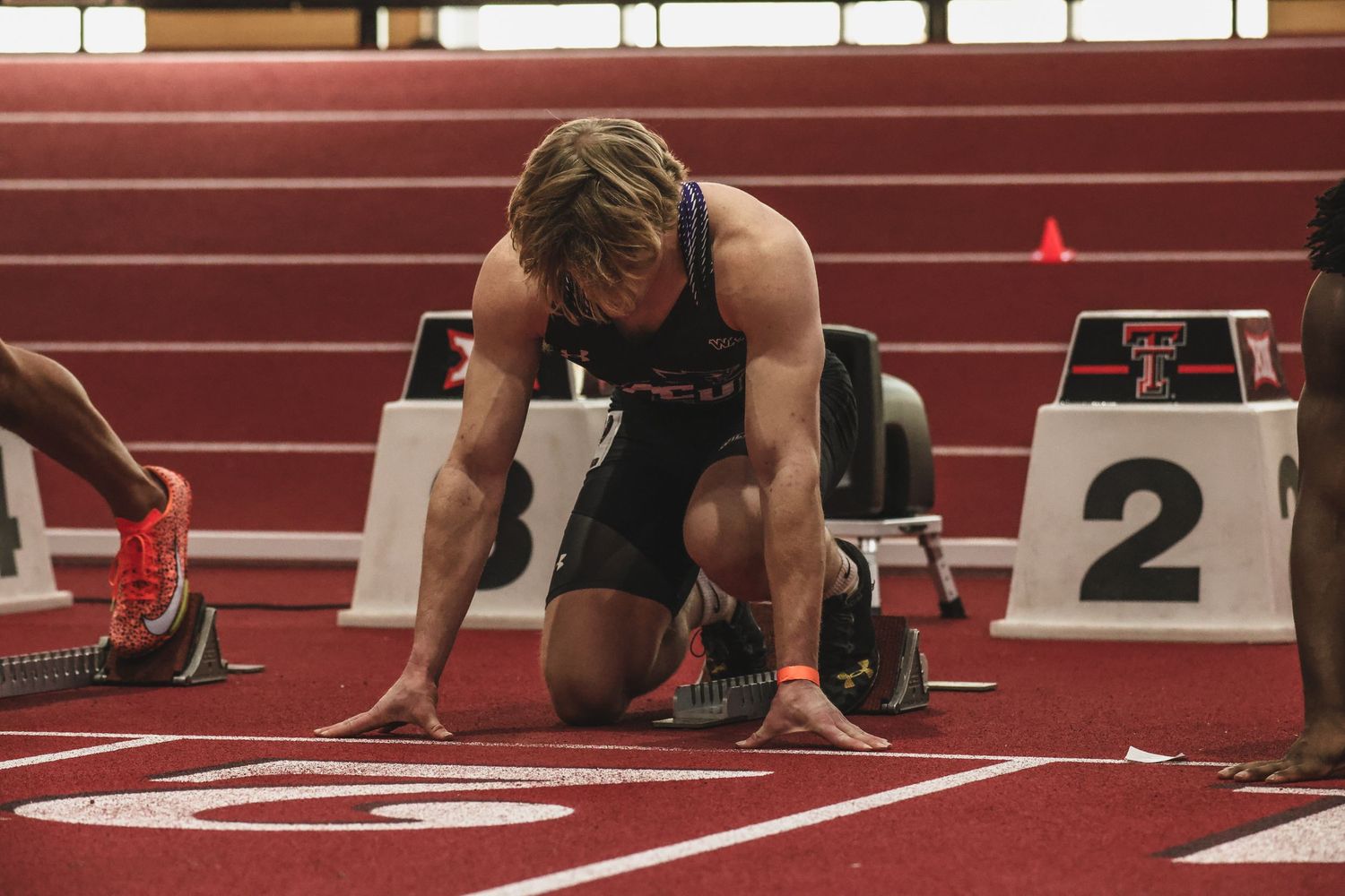 Athlete in starting blocks on indoor track at Texas Tech, preparing for sprint race.
