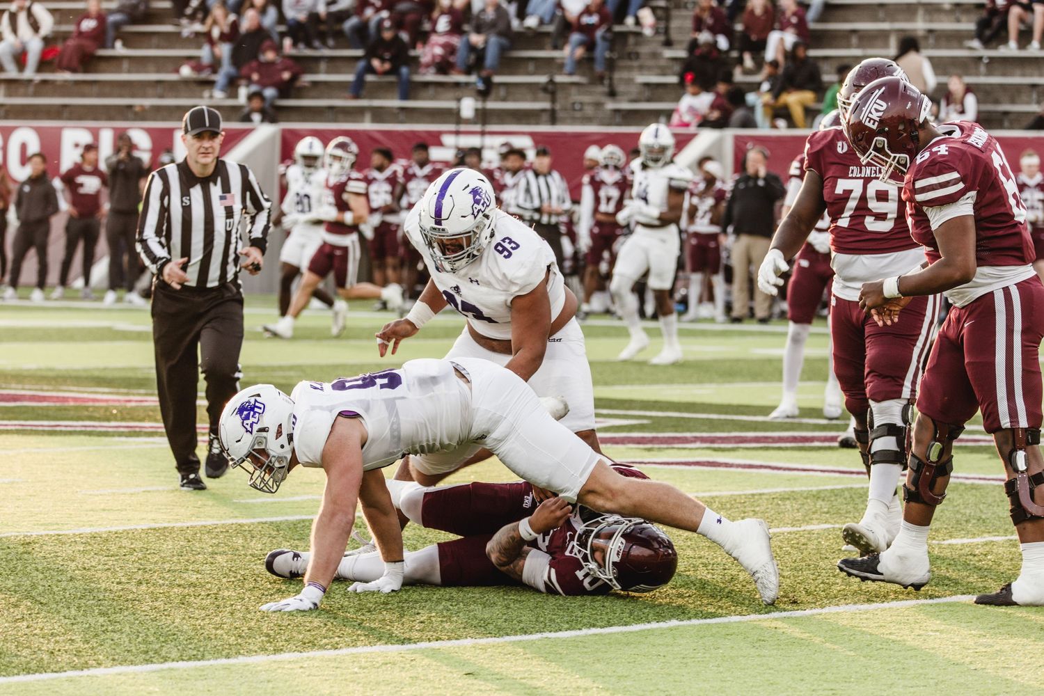 White-uniformed football player scores a touchdown while being tackled in an end zone.