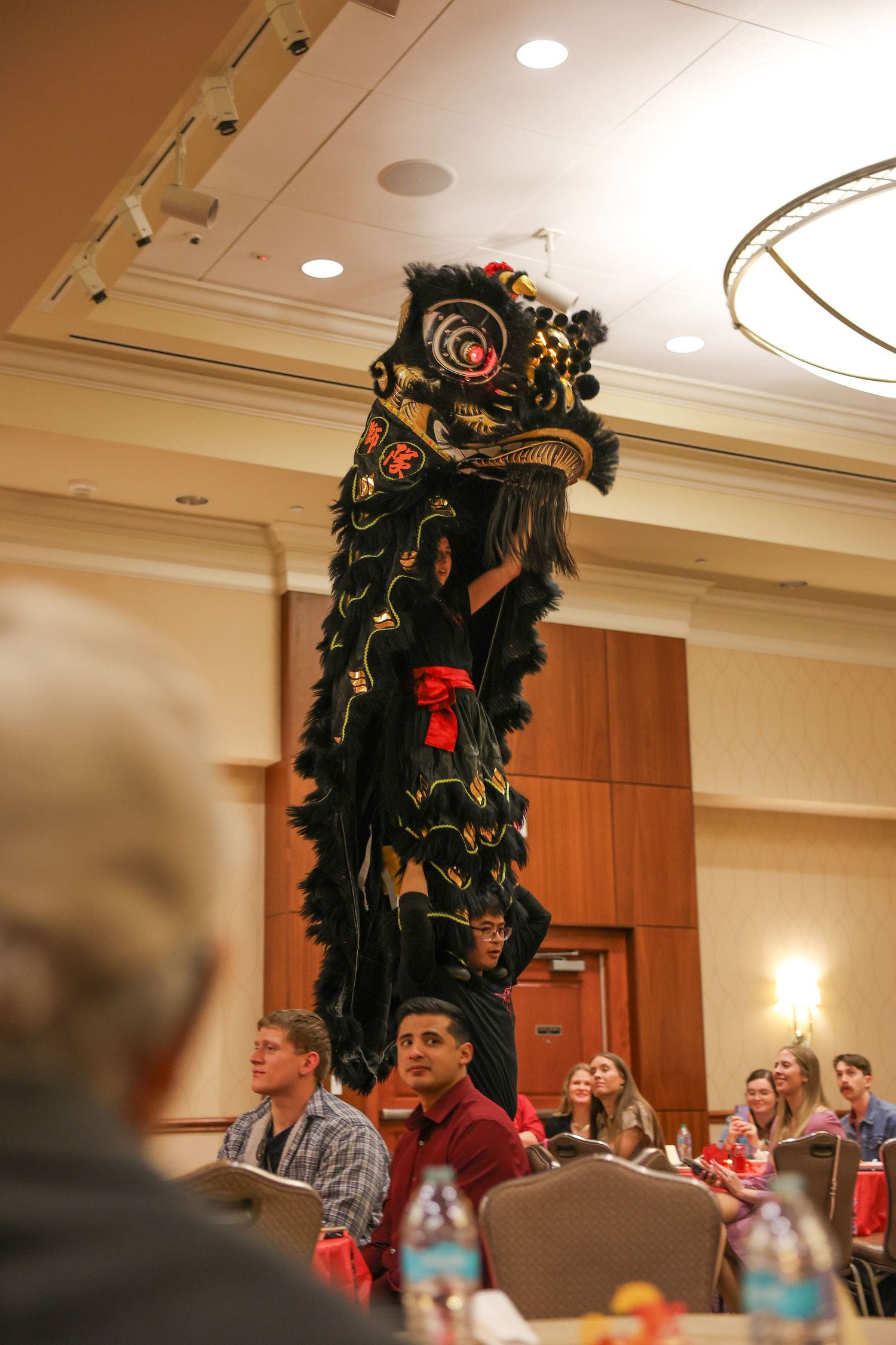 Performers executing impressive tall lion dance stunt before seated audience at cultural banquet.