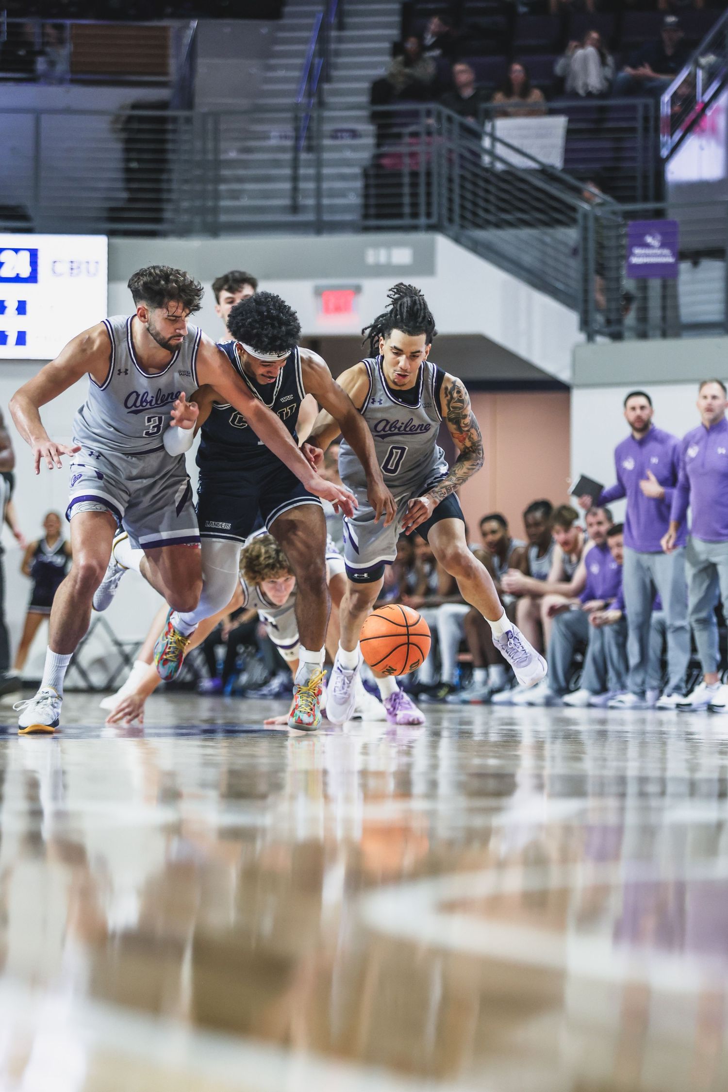Two Abilene Christian basketball players in white uniforms battle for a loose ball on the court.