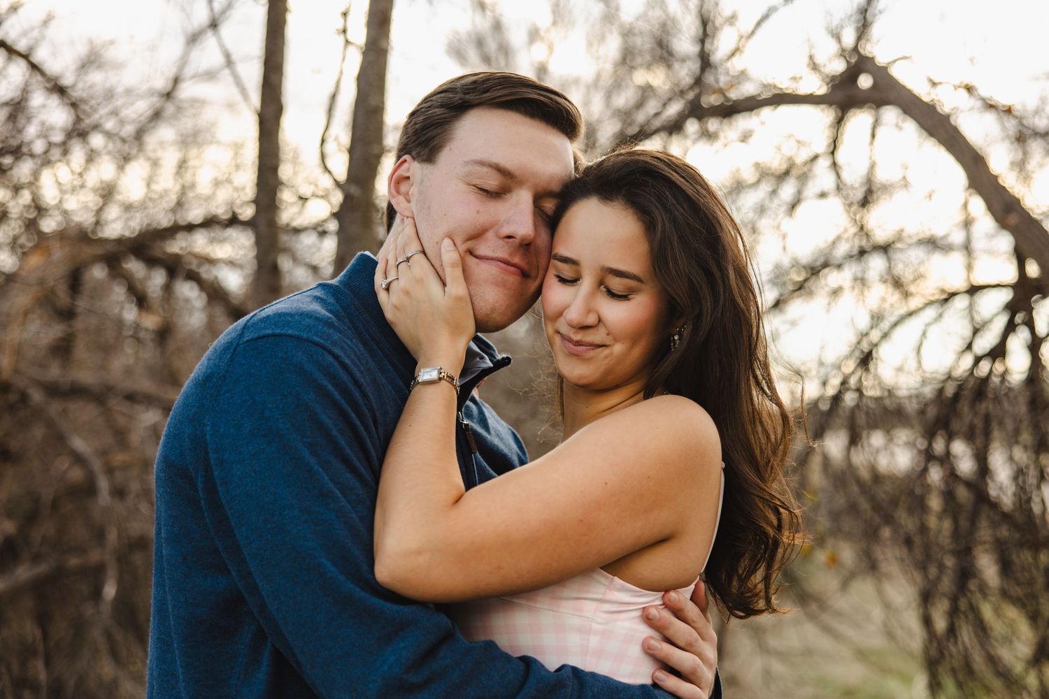 Romantic couple cuddling tenderly outdoors with soft golden hour lighting among trees.