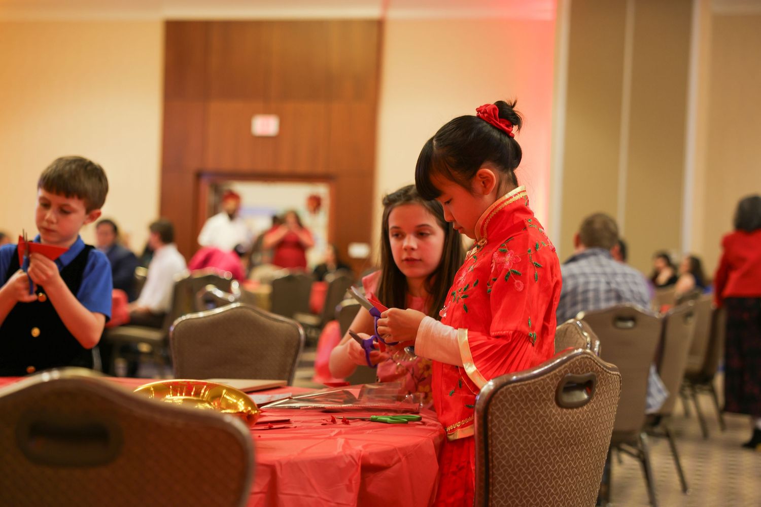 Young girl in red qipao dress participates in Chinese New Year craft activity at cultural event.