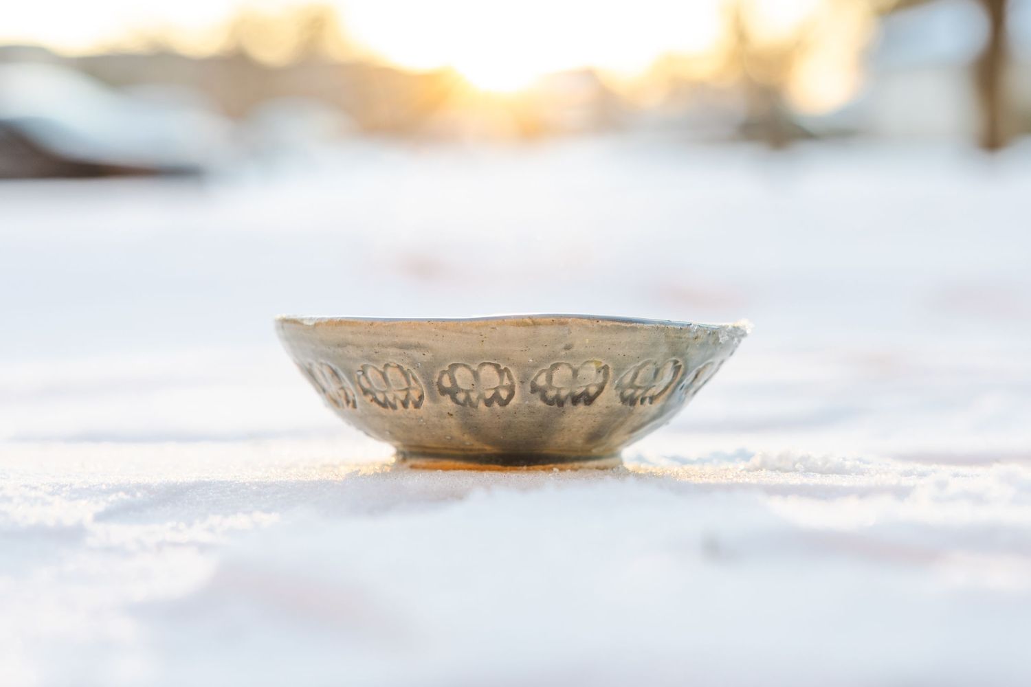 Ornate vintage silver bowl sitting in fresh white snow with warm bokeh background.