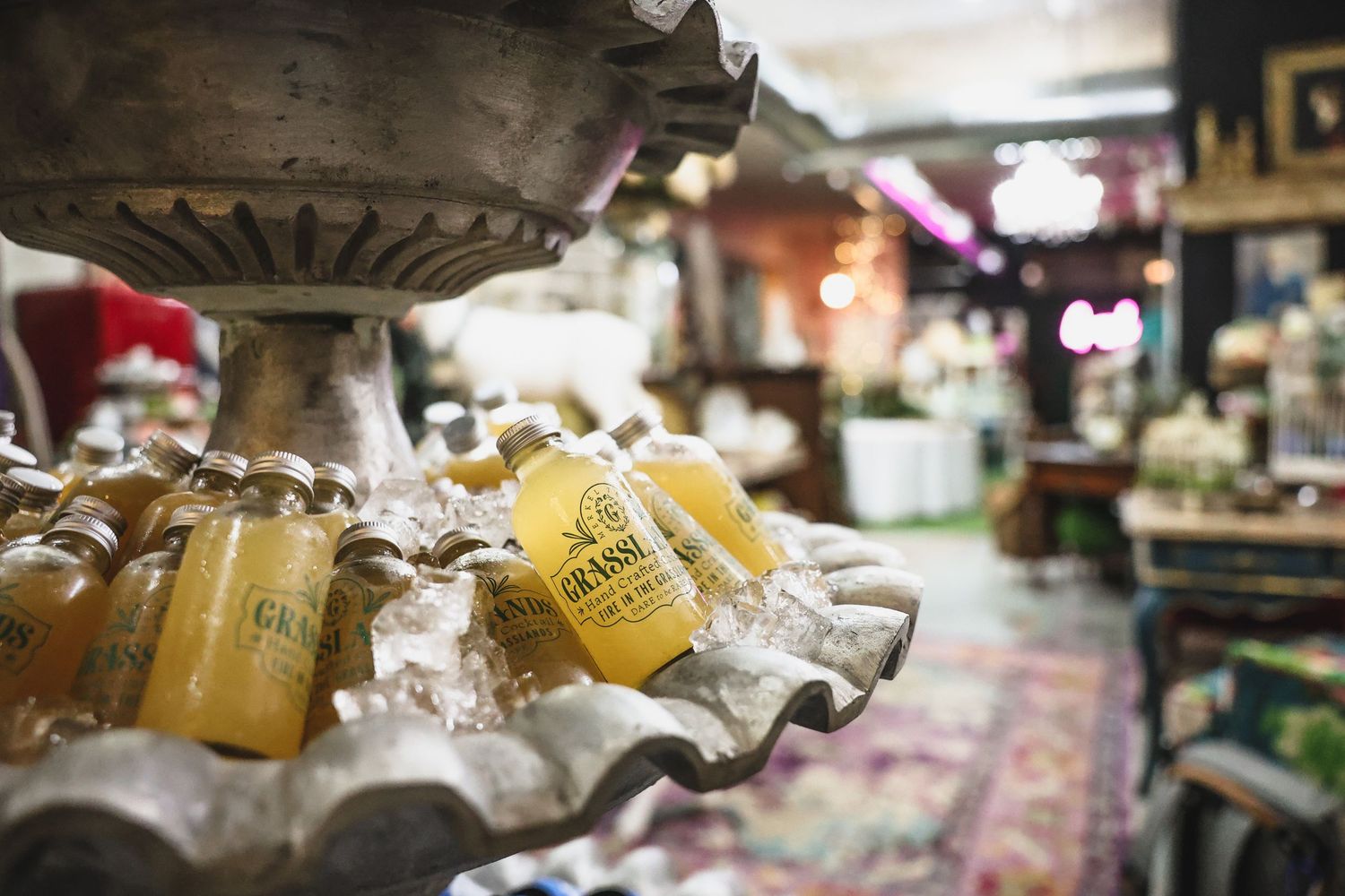 Grasslands branded yellow beverage bottles displayed on ice in ornate antique fountain bowl.