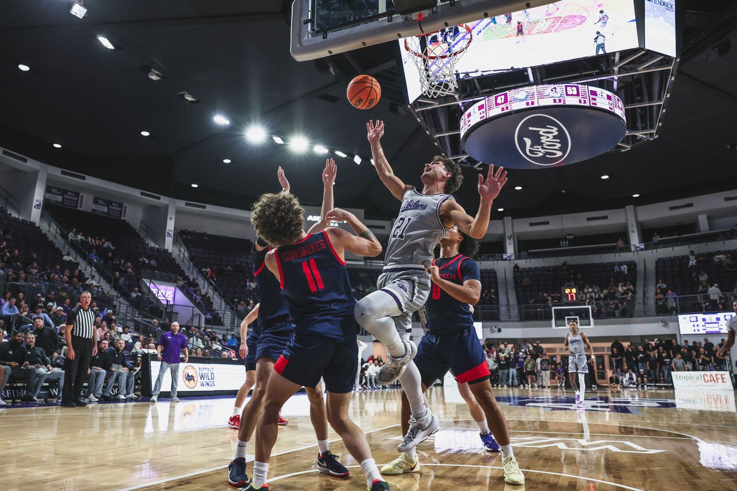Abilene Christian player attempts a layup through contact against Texas Tech defenders in college basketball.
