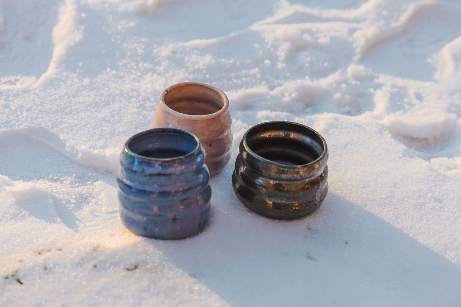 Three handmade ceramic bowls with colorful glazes resting in white snow outdoors.