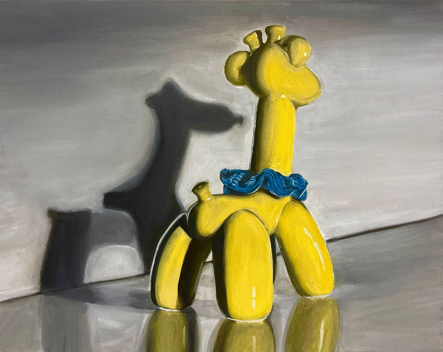 A glossy yellow balloon giraffe figurine with a blue bow tie casting a shadow on a gray surface.