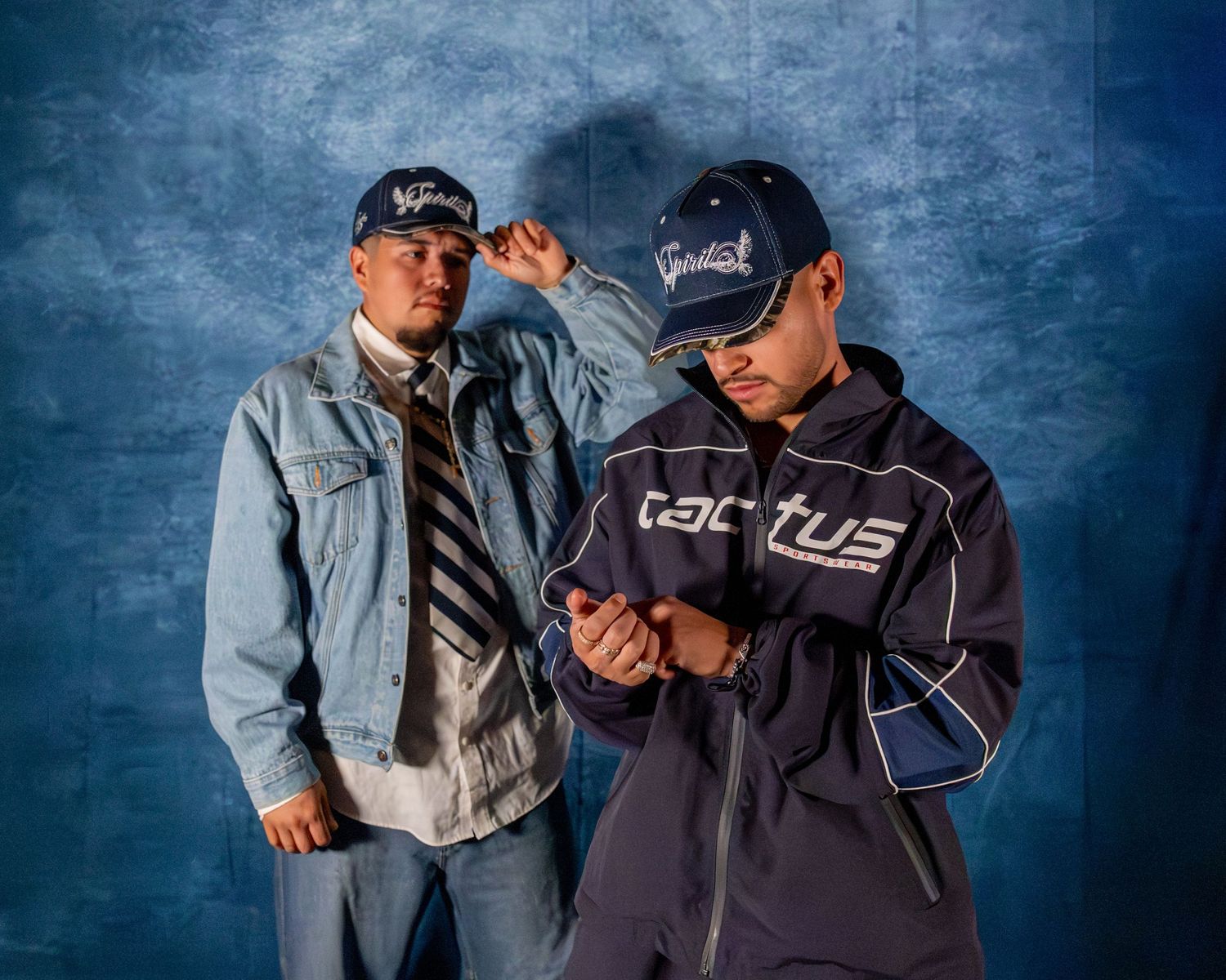 Two men in Spirit caps pose in denim and Cactus jacket against blue studio background.