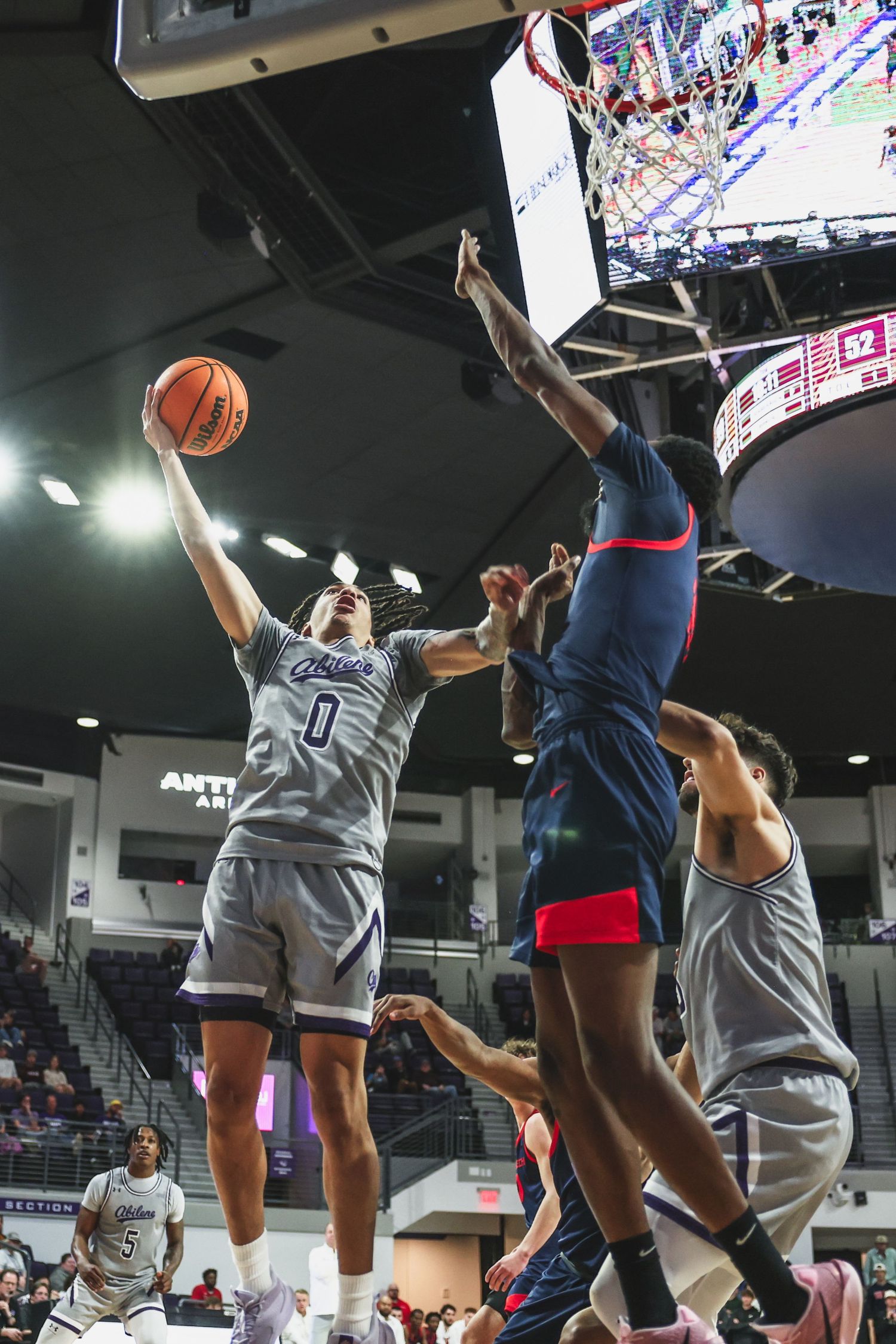 Abilene Christian player number 0 goes up for a layup against Texas Tech defenders in college basketball.