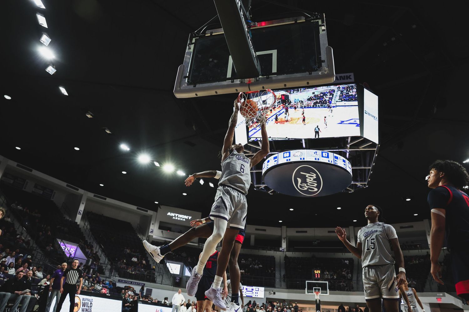 A college basketball player executes a powerful dunk over a defender during an exciting indoor arena game.