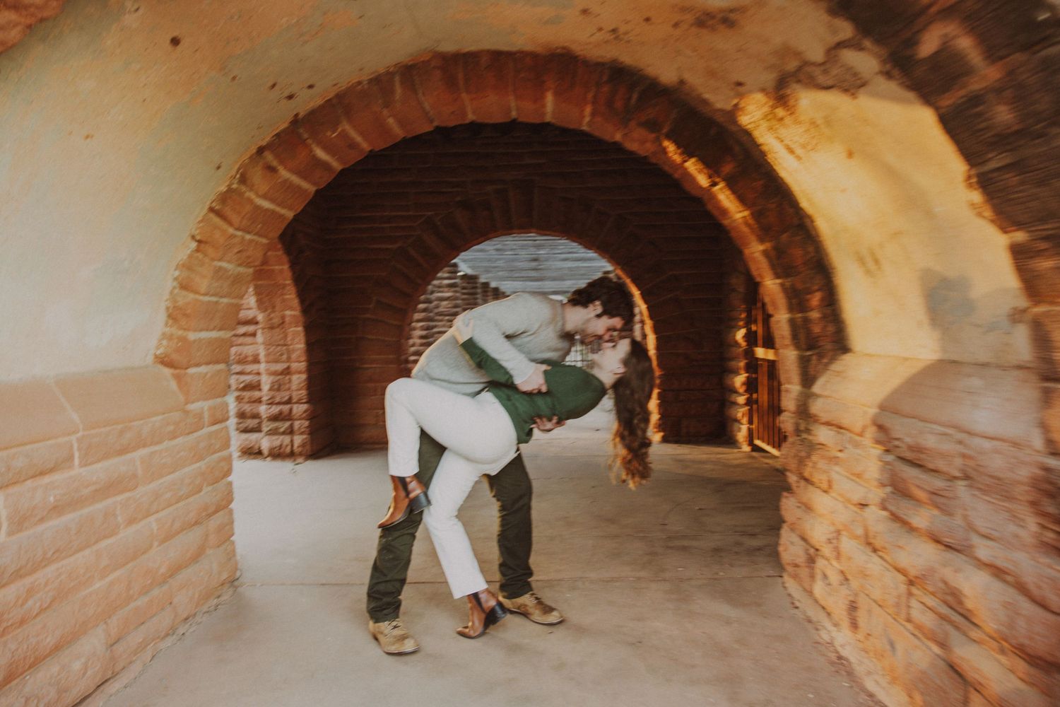 Couple sharing a romantic dip kiss inside a beautiful brick arched tunnel walkway.