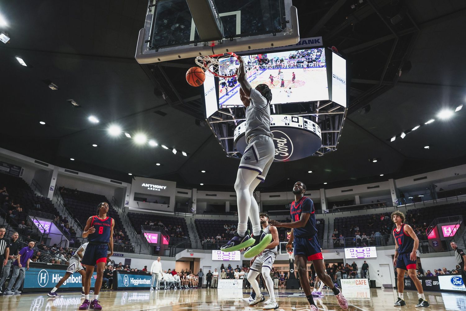 Athletic basketball player dunking the ball with opponents watching below in a college arena game.