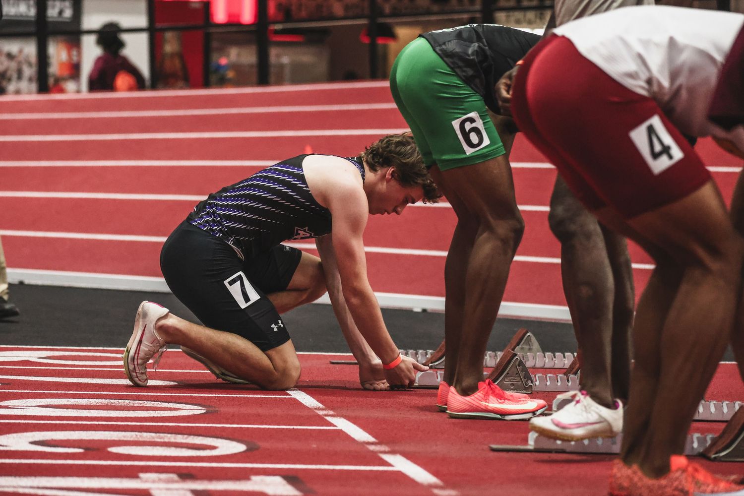 Athletes prepare in starting blocks for indoor track sprint race.