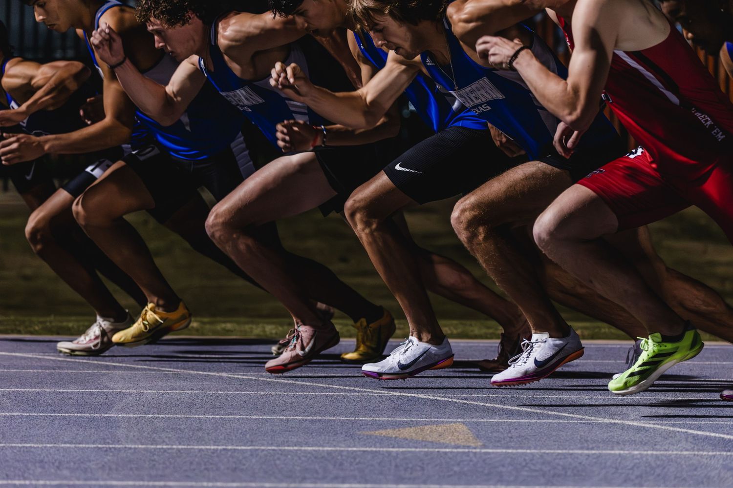 Male sprinters explode off starting blocks at beginning of track race.