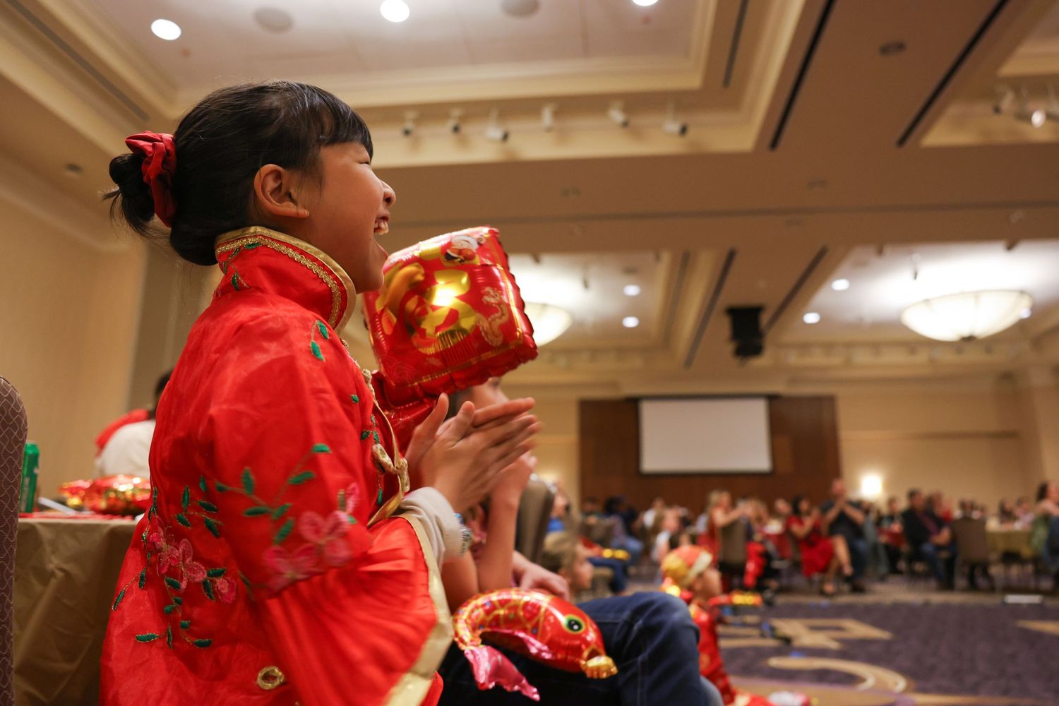 Young girl in red traditional Chinese dress holds illuminated lantern at Lunar New Year banquet.