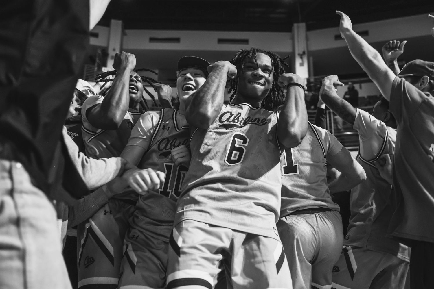 Basketball player number 6 celebrates with teammates in an energetic black and white victory photo.
