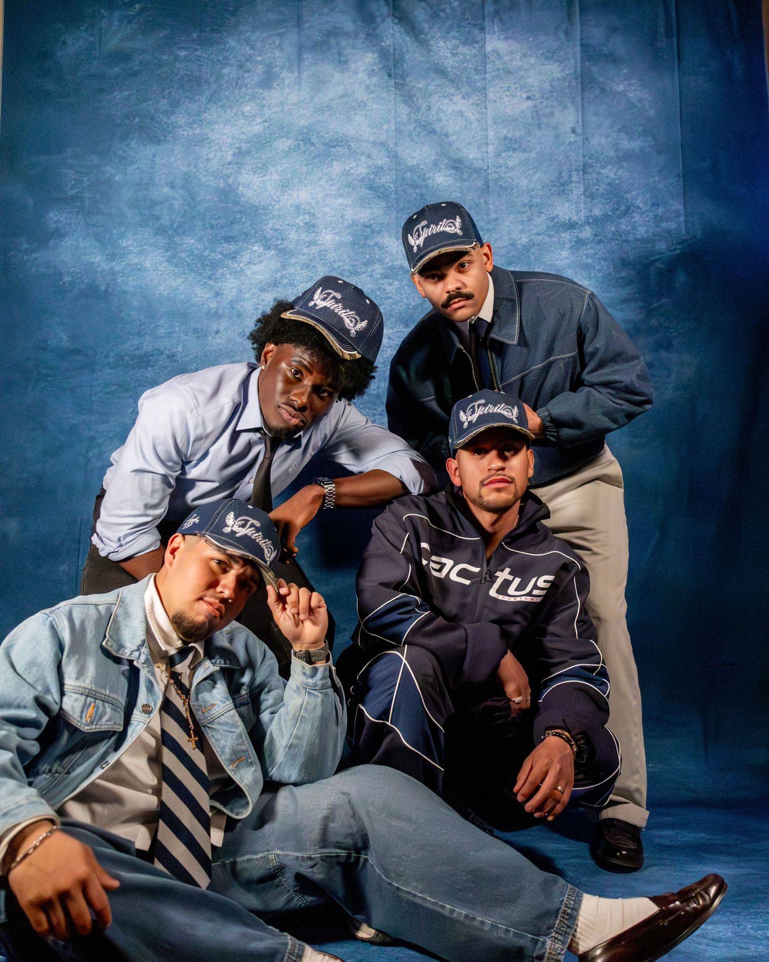 Four men pose together in matching navy caps for a stylish urban group photo shoot.