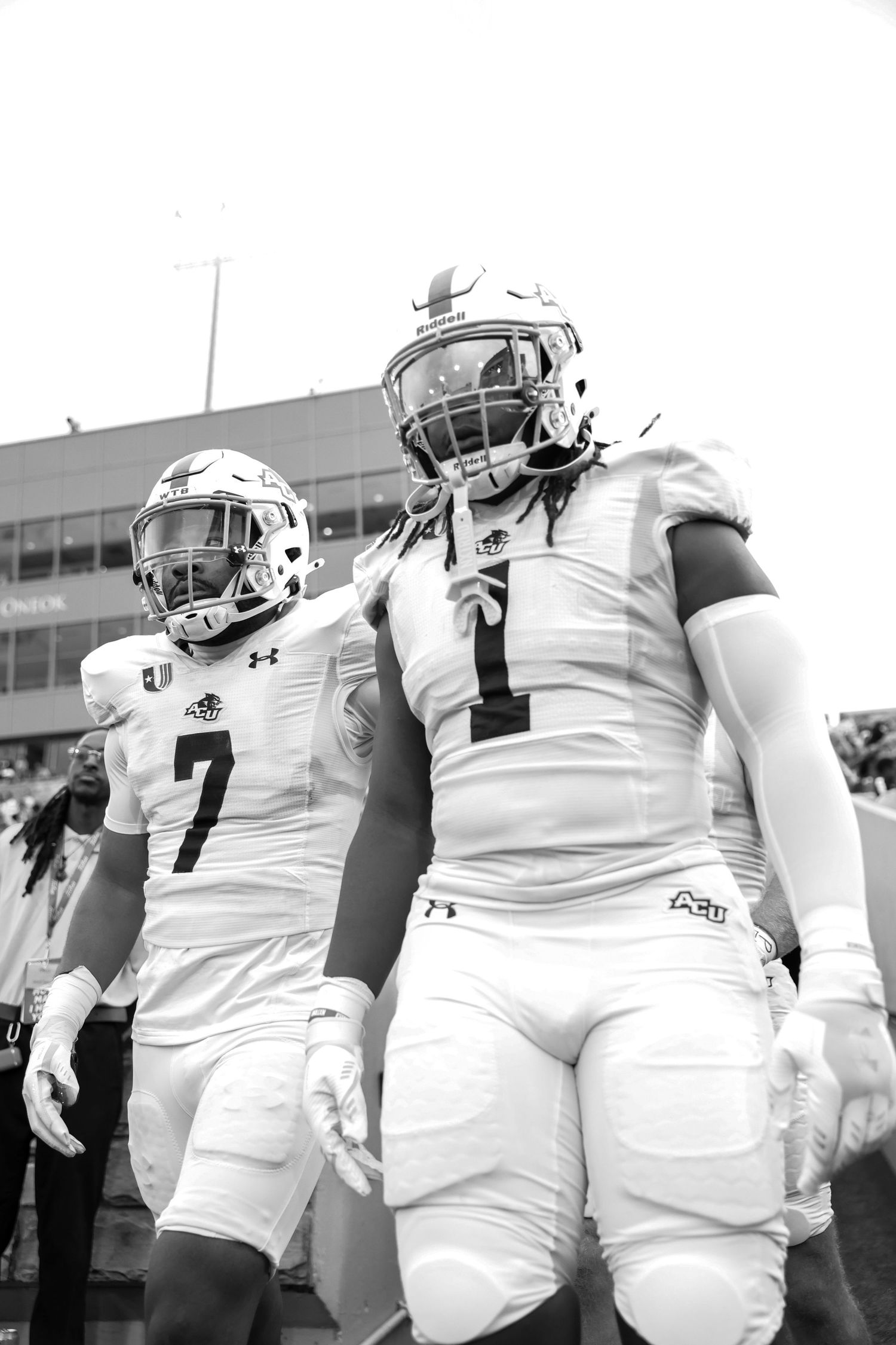 Two college football players in white uniforms walk onto the field in a black and white photo.