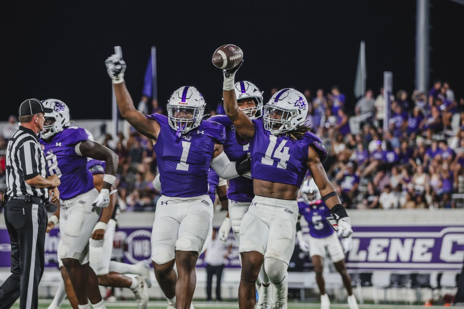 College football players in purple uniforms celebrate a score during a night home game.