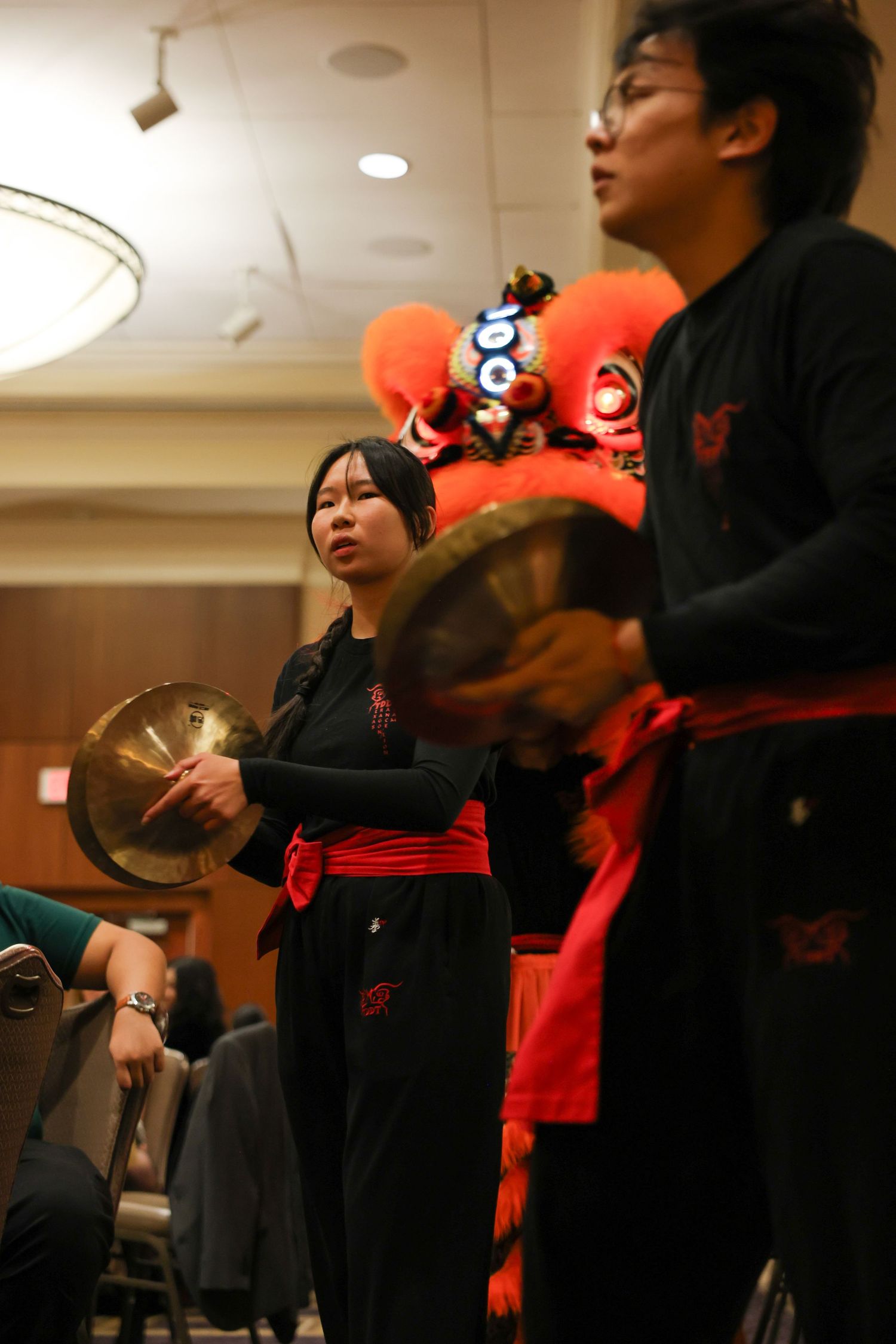 Musicians in black and red play cymbals during a traditional Chinese lion dance cultural performance indoors.