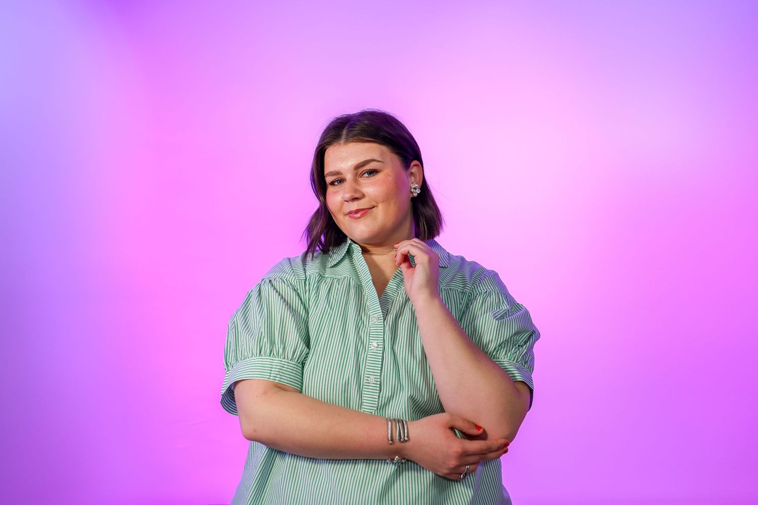 Smiling plus-size woman in mint green shirt poses against vibrant pink and purple background.