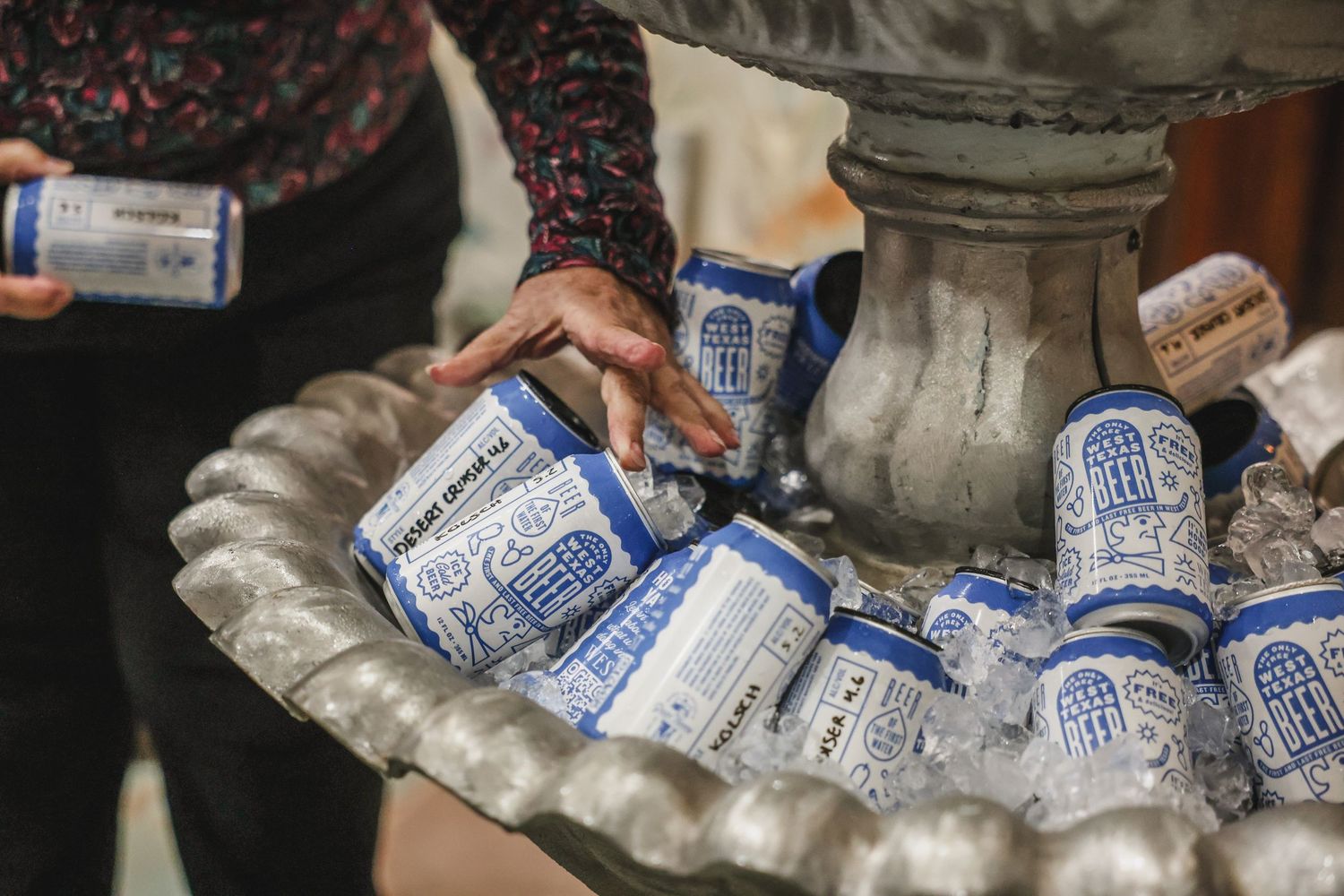 Person grabbing canned beverages from an ice-filled decorative stone fountain.