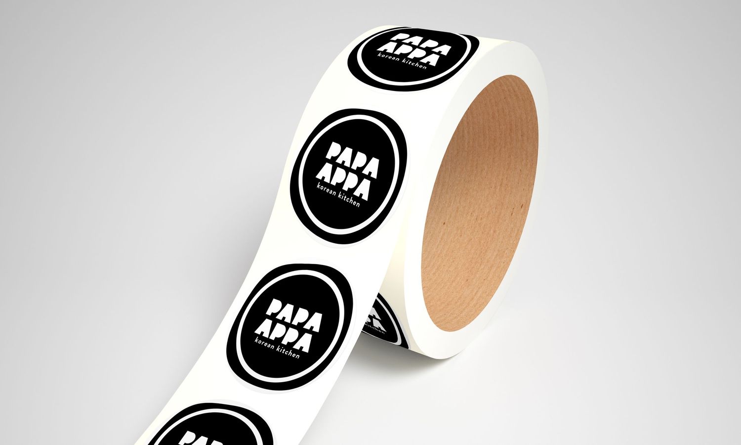 Roll of round black and white Papa Appa Korean Kitchen stickers on a neutral gray background.