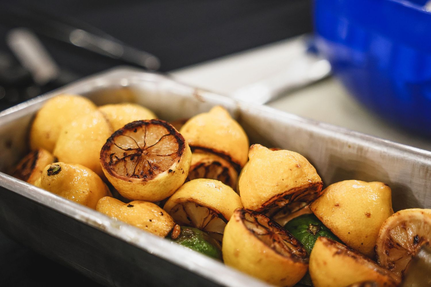 Roasted lemons and vegetables in a metal baking pan for catering preparation.
