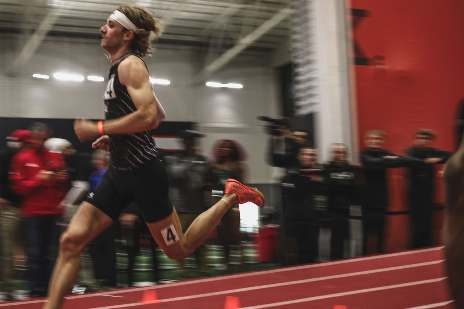 Male runner sprints at full speed during indoor track and field meet.