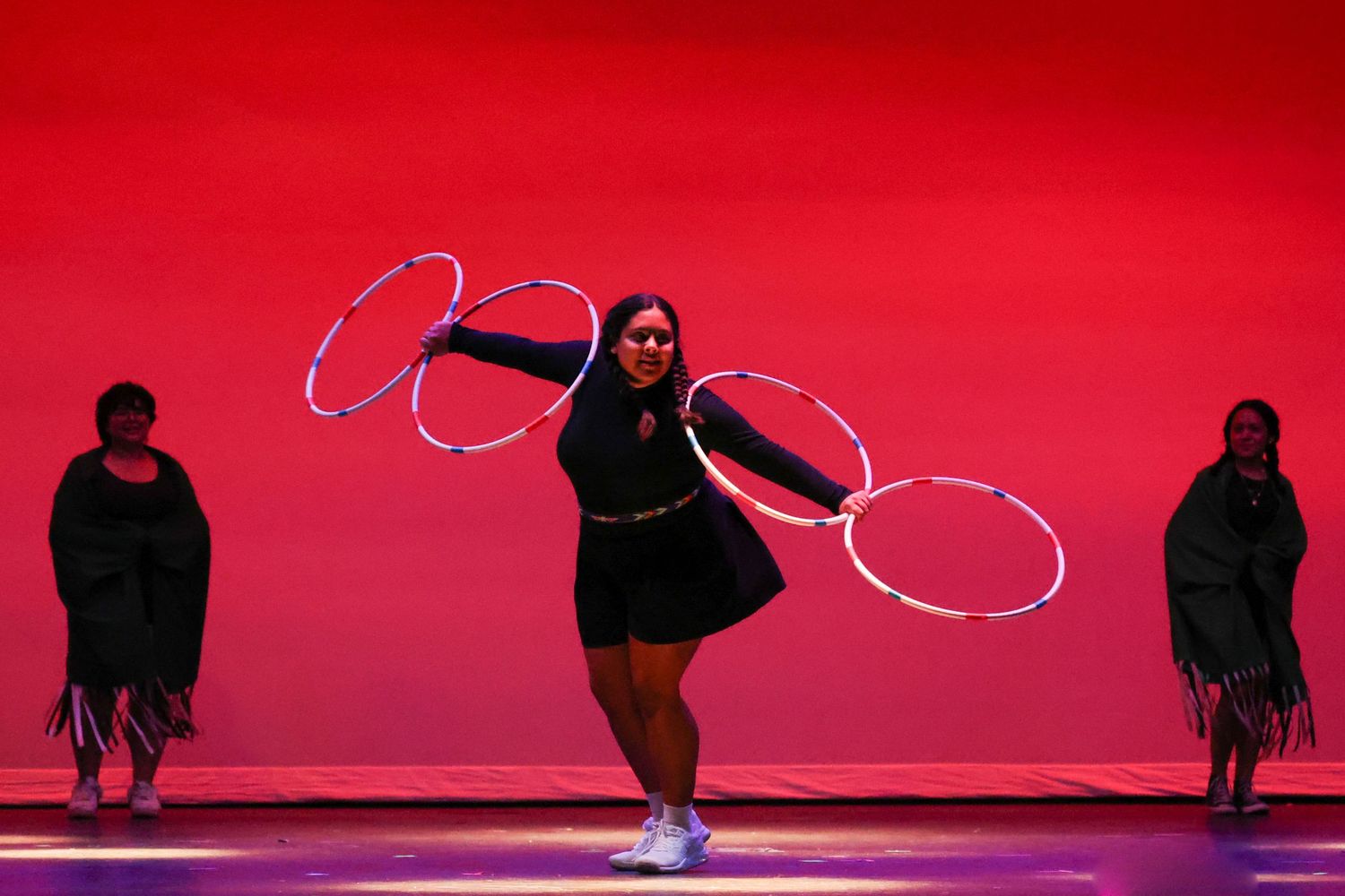 Performer spins multiple illuminated hula hoops on a red-lit stage during a captivating cultural dance show.