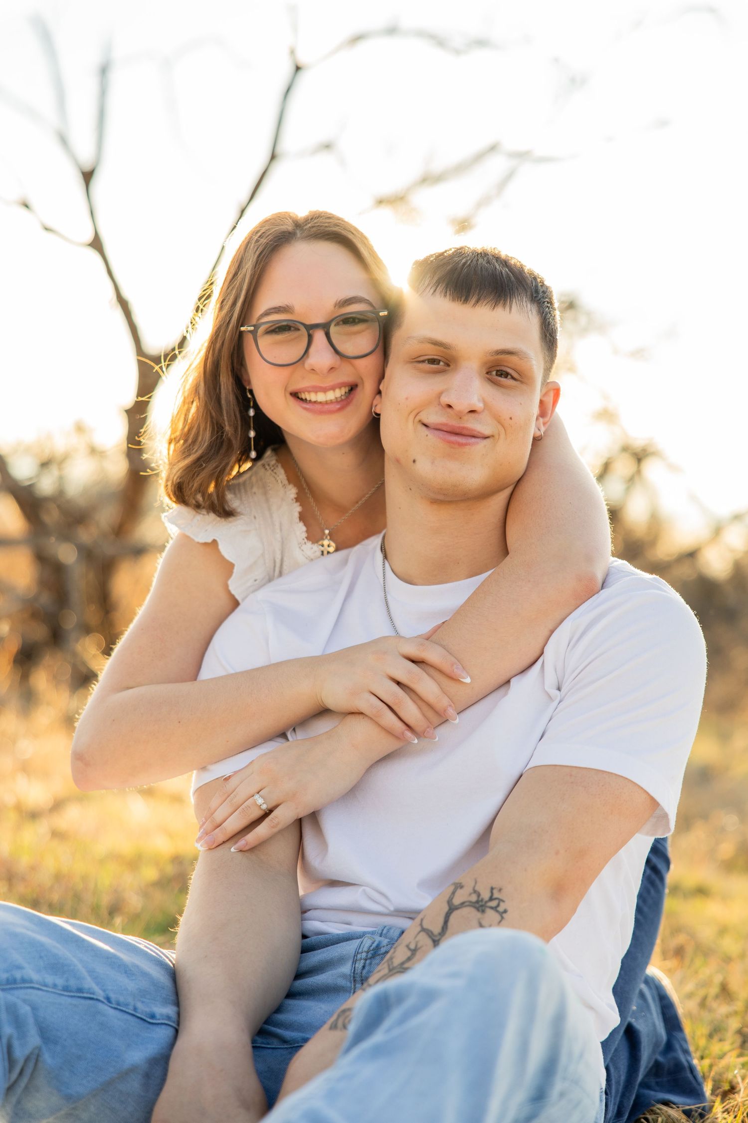 Smiling couple embracing warmly outdoors in a sun-drenched field during golden hour.