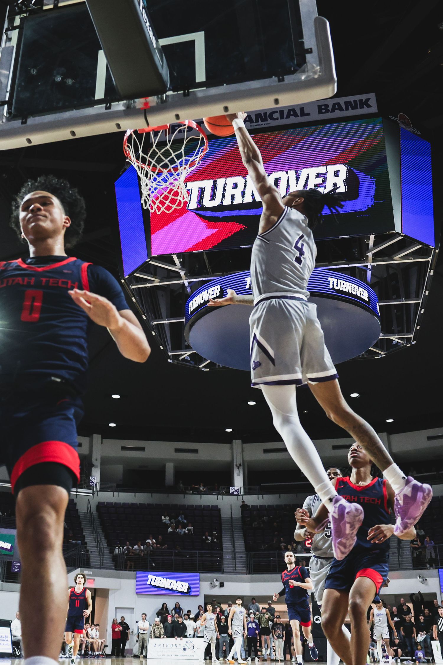 Basketball player dunks over defenders as the scoreboard displays TURNOVER in a college arena game.
