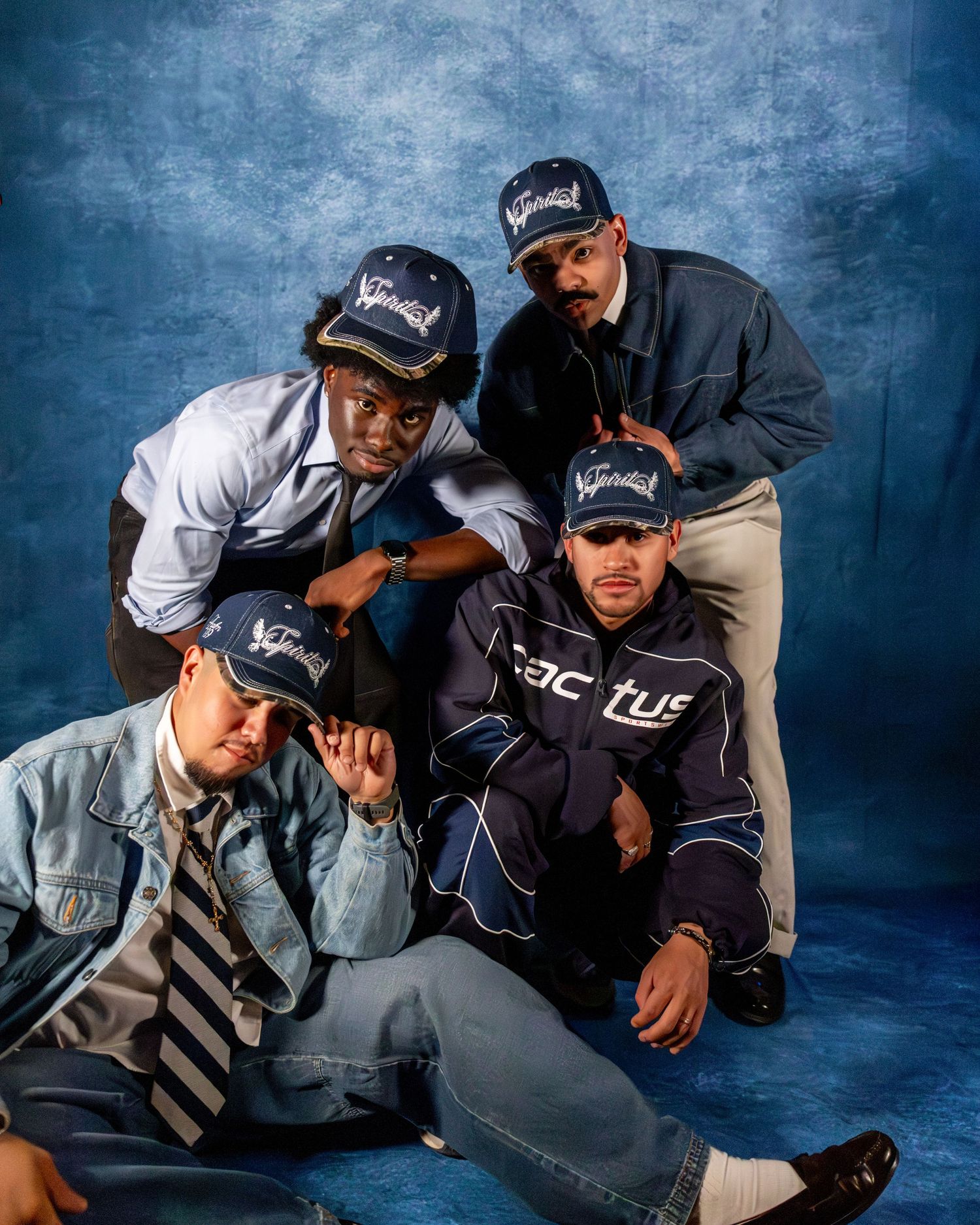 Group of four men posing together wearing matching caps in a blue-toned studio portrait.
