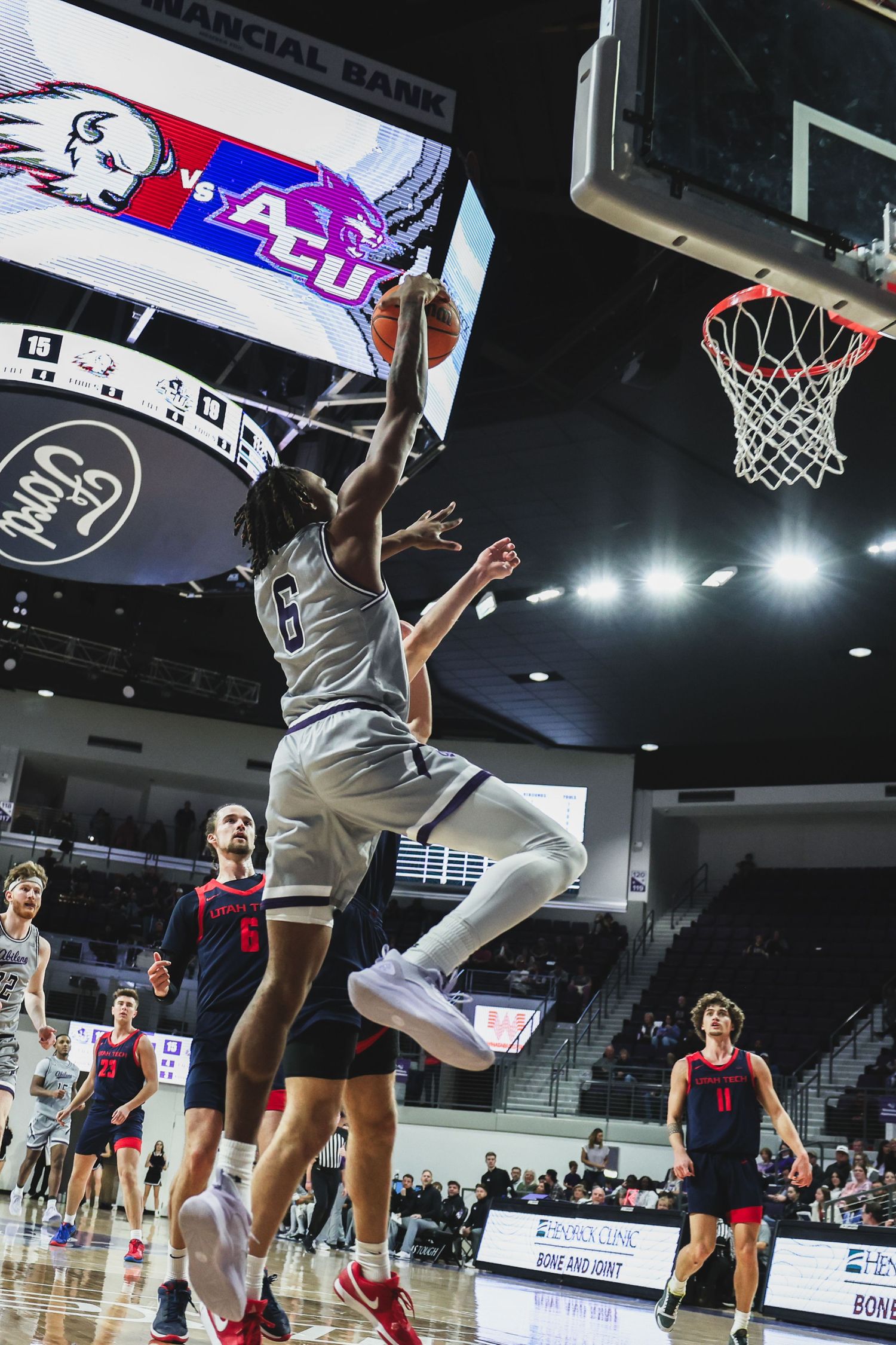 College basketball player wearing number 6 dunks over a defender in a brightly lit indoor arena.