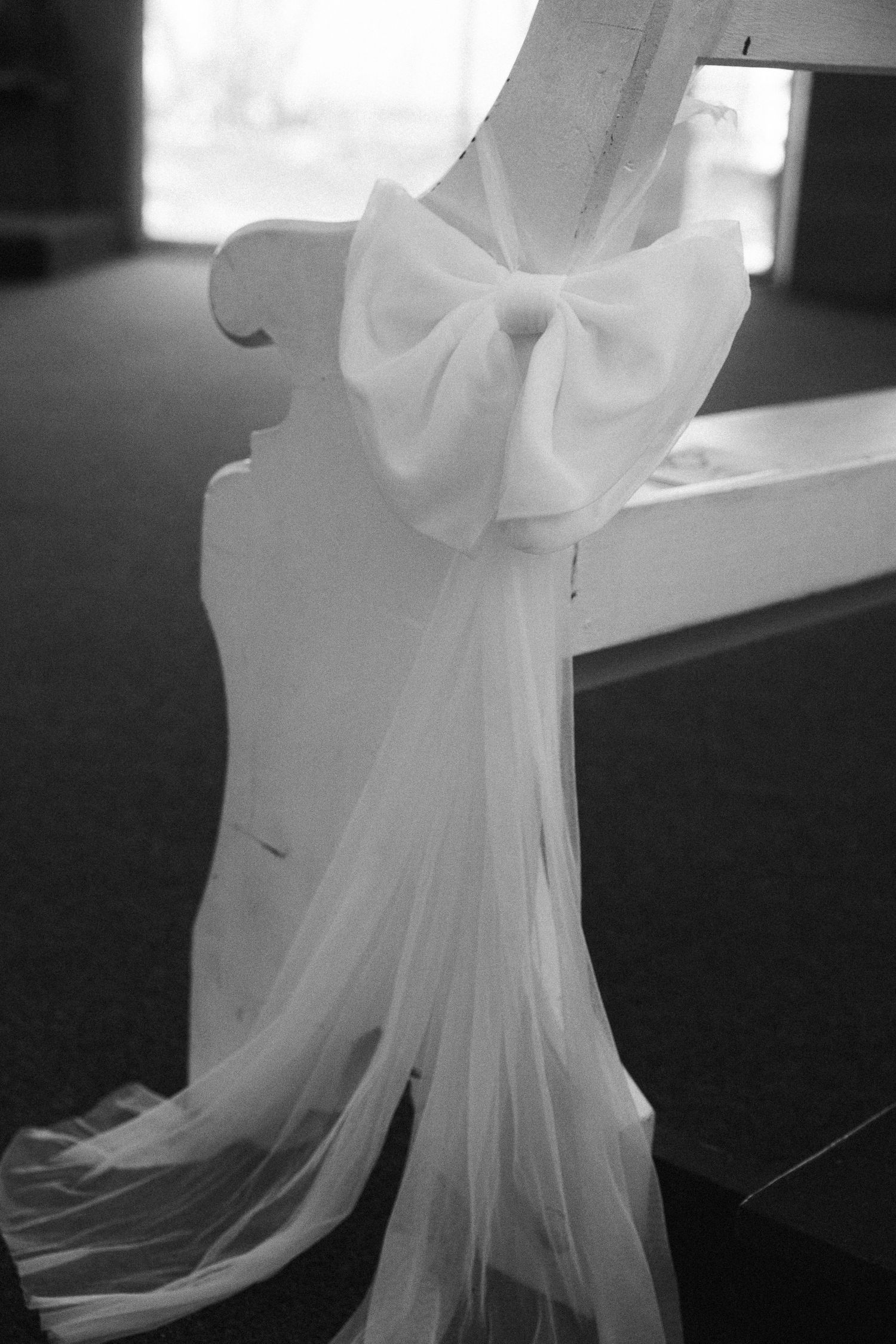 White tulle bow decoration on wedding ceremony church pew in black and white photo.