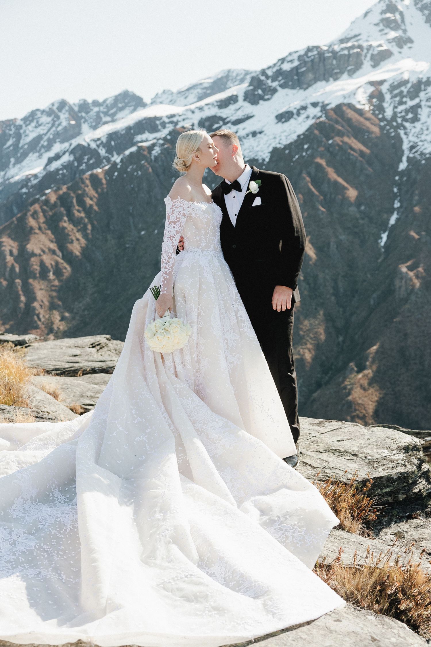 Bride and groom kissing on mountain top with snow-capped peaks in Queenstown New Zealand.