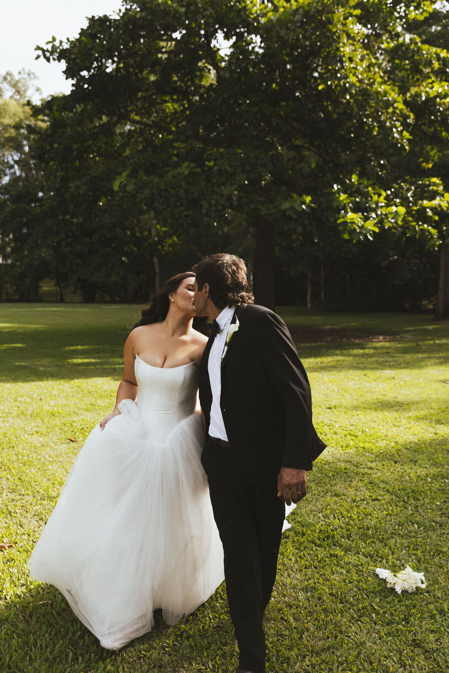 Bride and groom sharing a romantic kiss in a lush green garden setting.