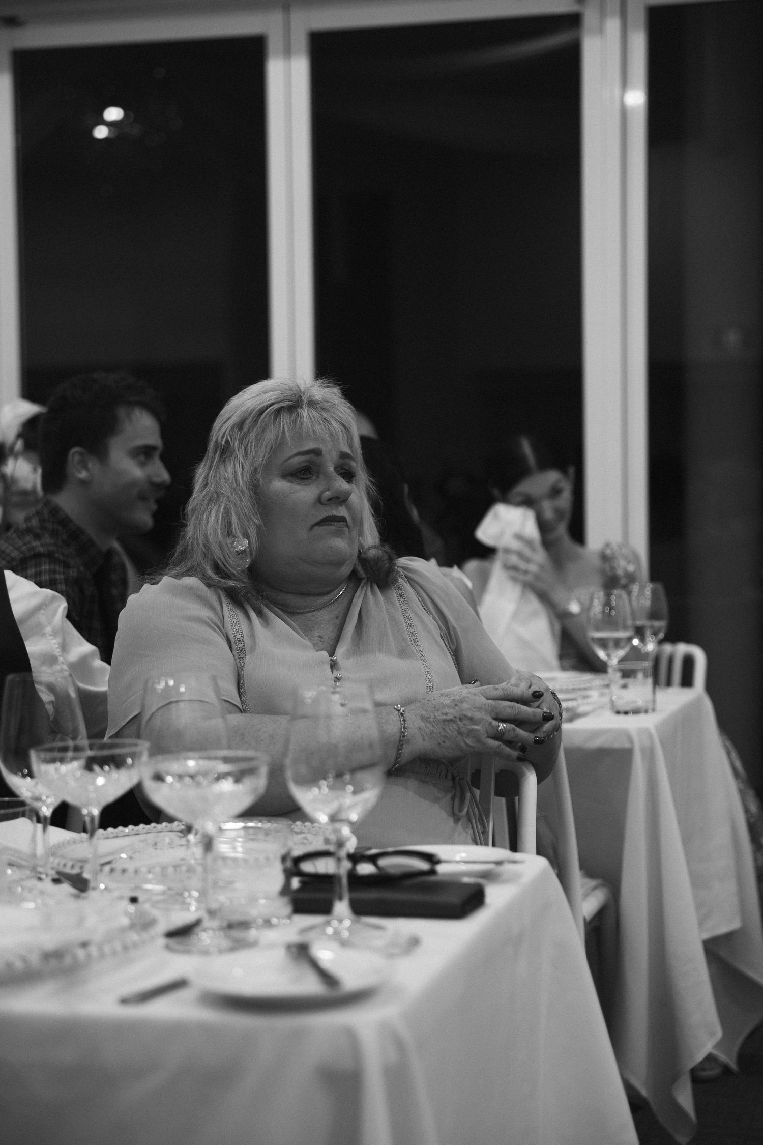 Black and white photo of blonde female wedding guest seated at elegantly set reception table.