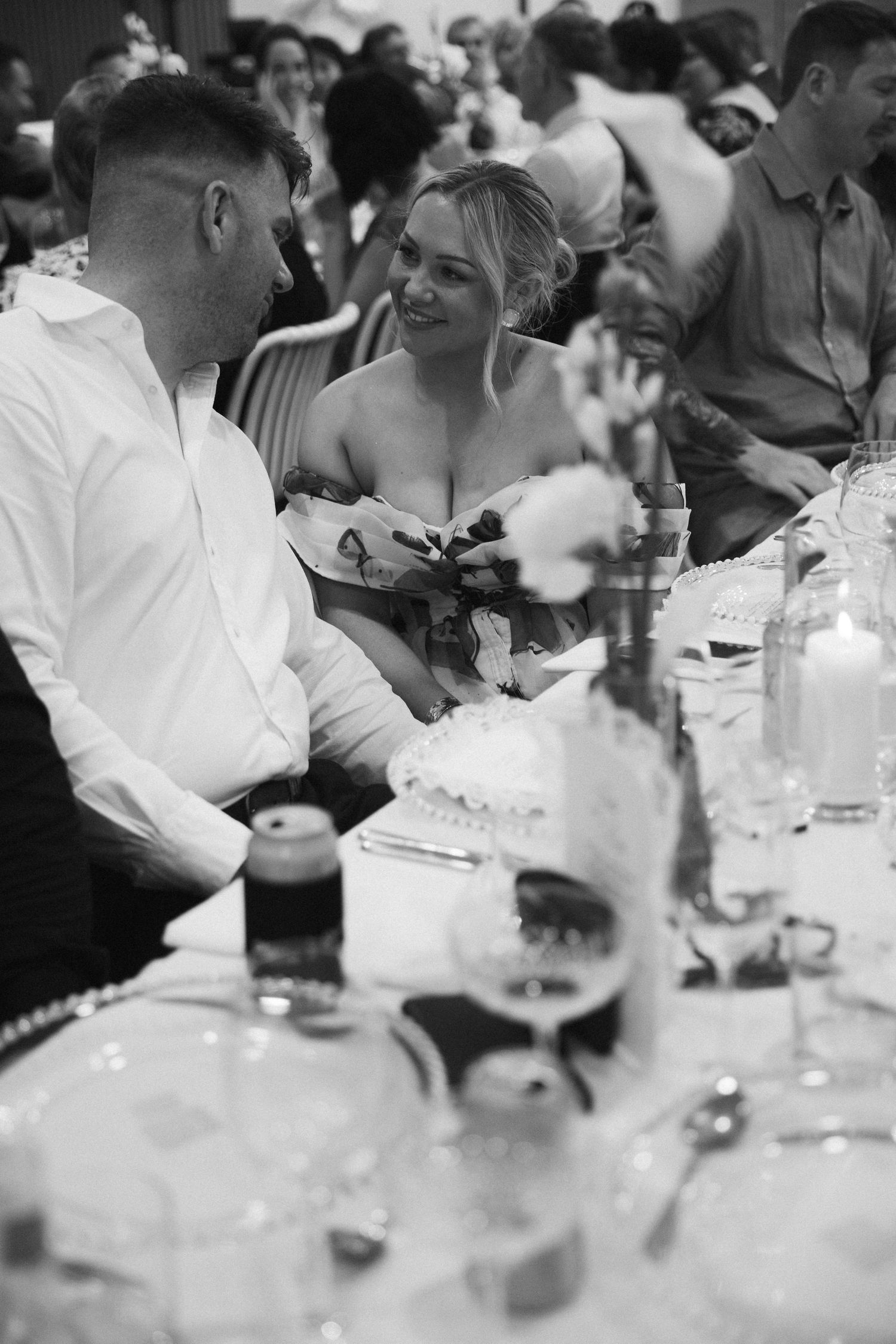 Black and white photo of wedding guests laughing together at wedding reception dinner table.