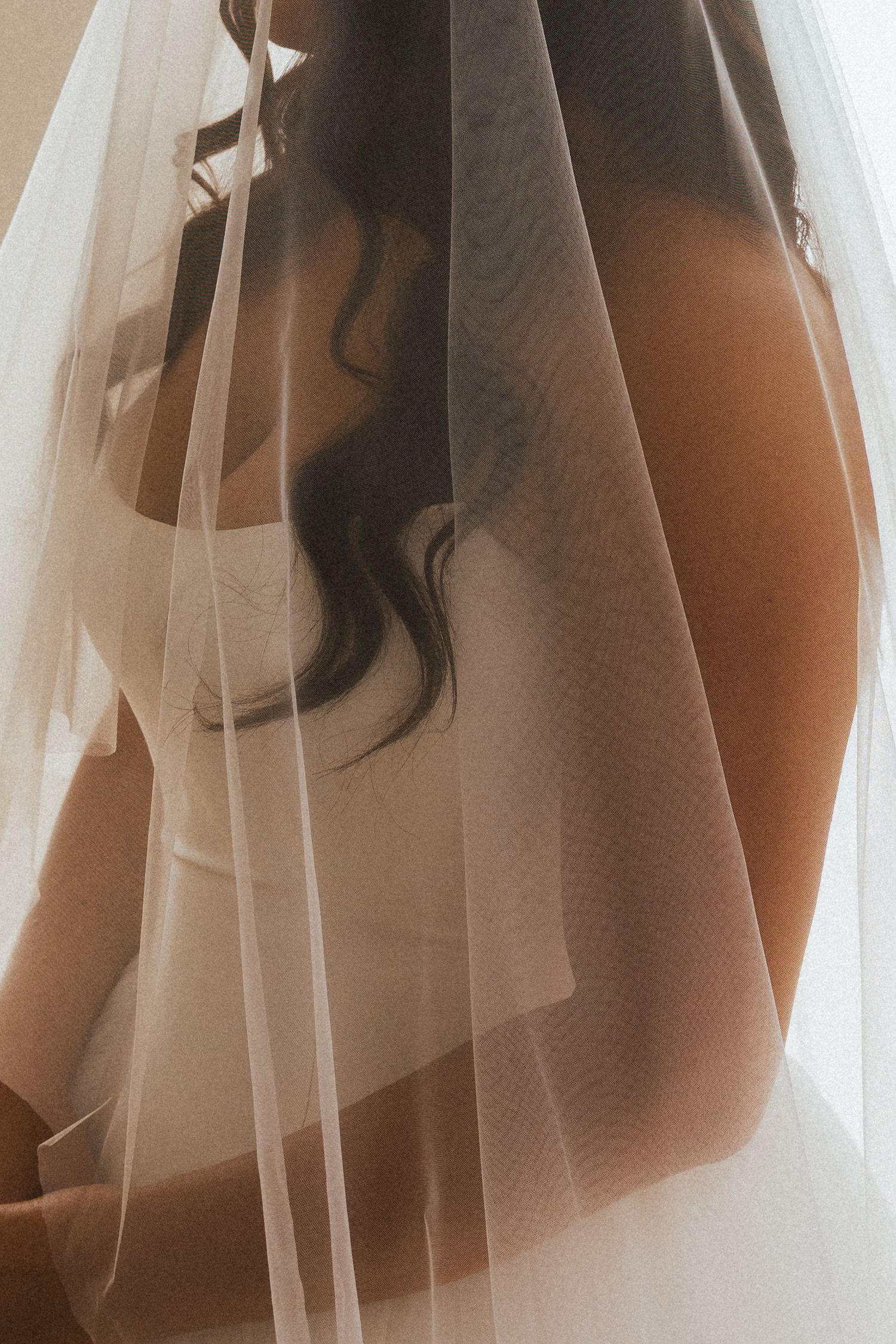 Close-up artistic shot of bride in white corset gown with sheer cathedral veil in warm light.