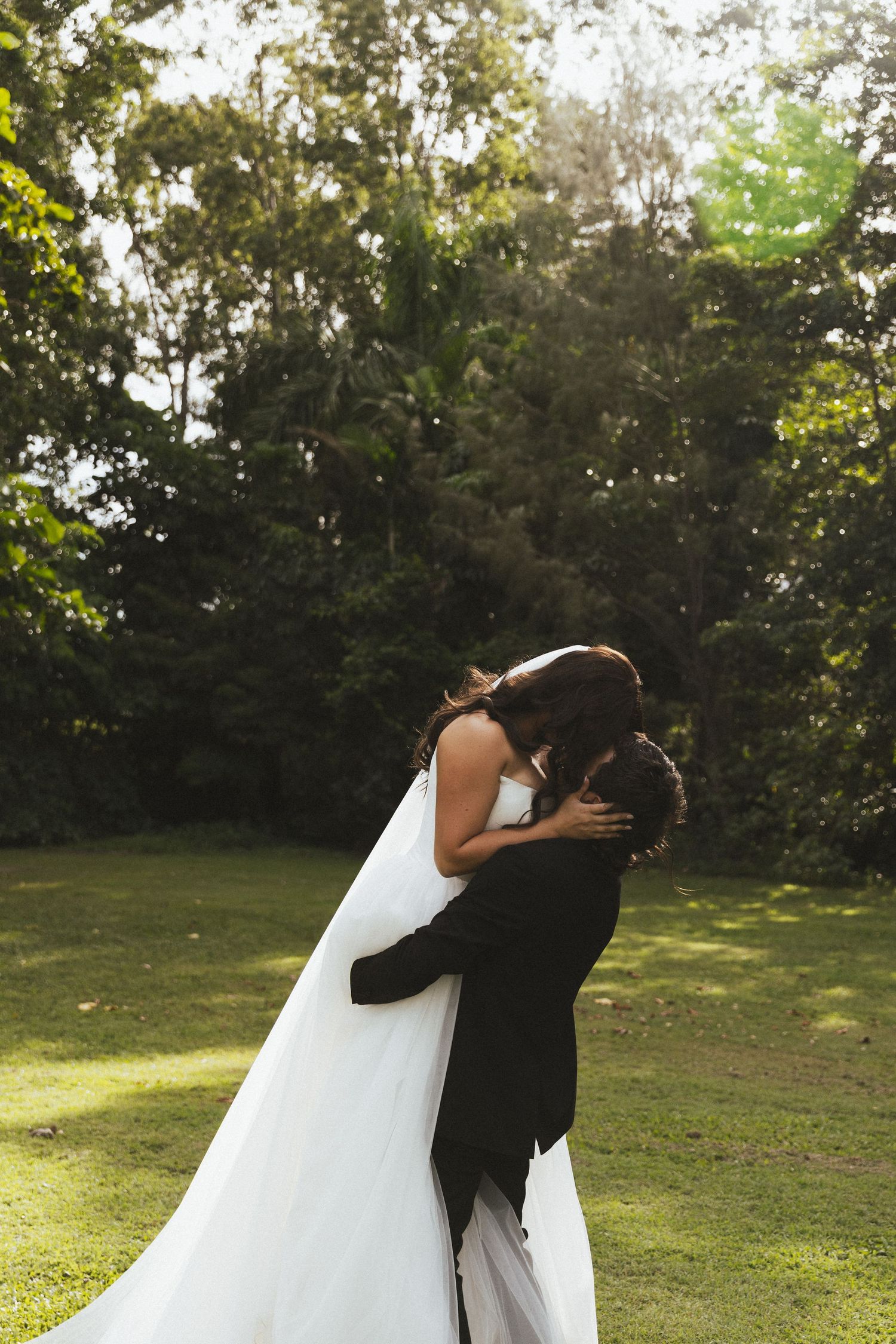 Bride and groom sharing romantic kiss in lush green garden setting on their wedding day in Whitsundays, Queensland.