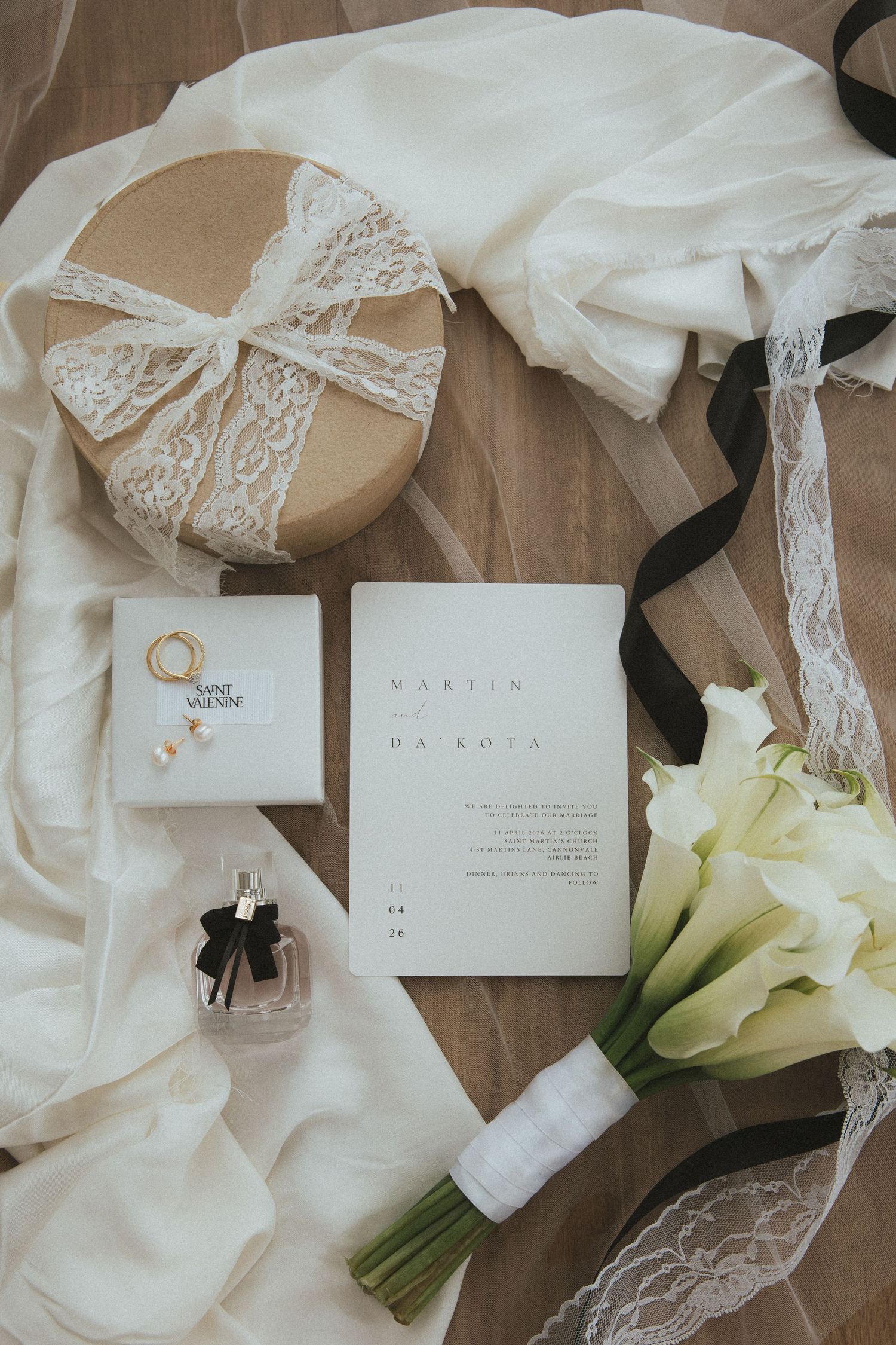 Elegant wedding flat lay with white calla lily bouquet, invitation suite, perfume bottle and lace gift box.