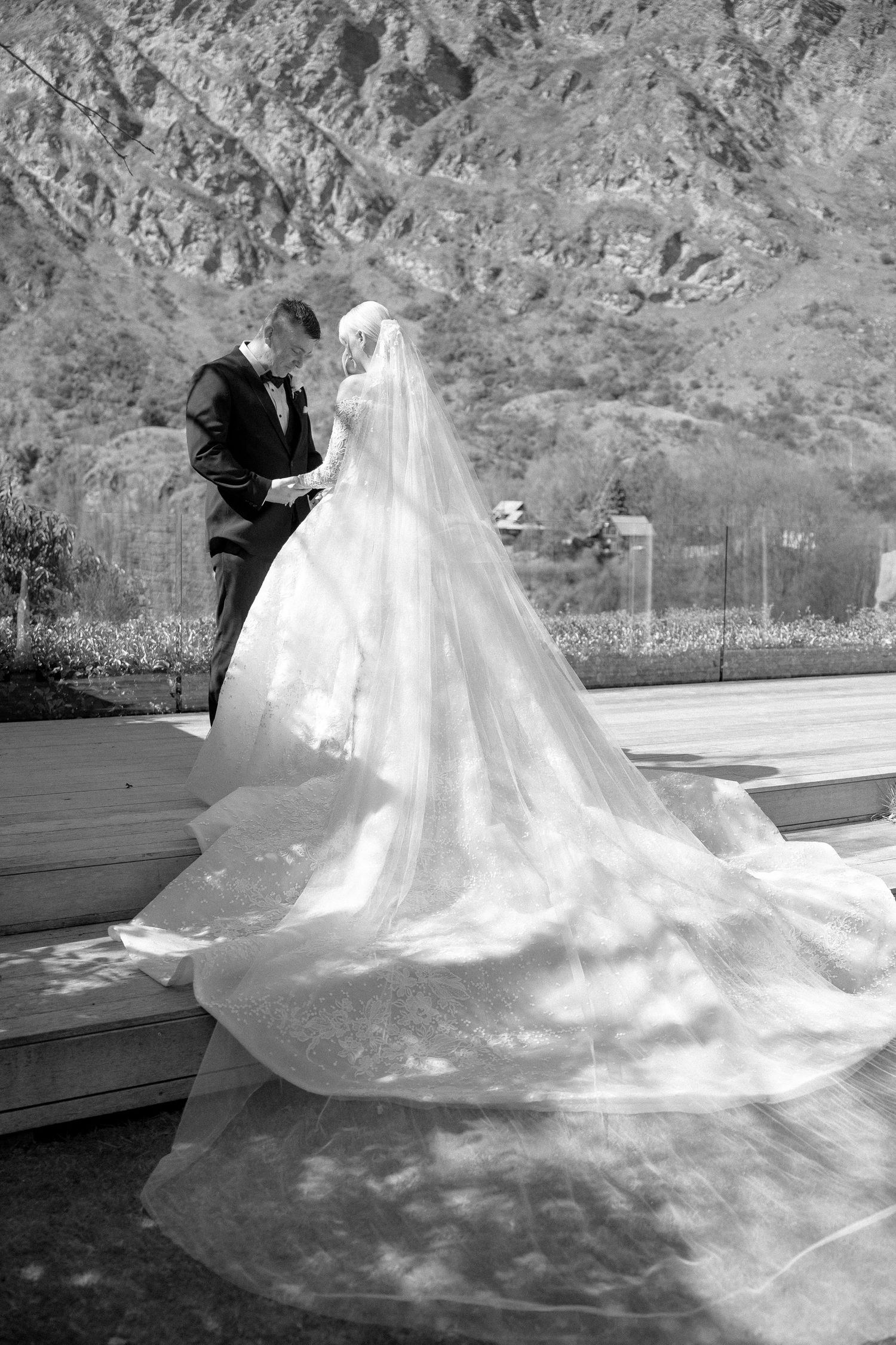 Bride and groom share intimate moment with stunning cathedral veil train spread on steps in mountains.