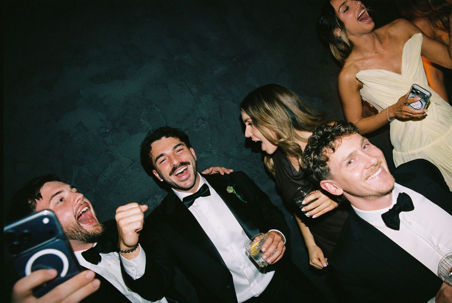 Groomsmen in tuxedos laugh and celebrate together at a wedding reception party.