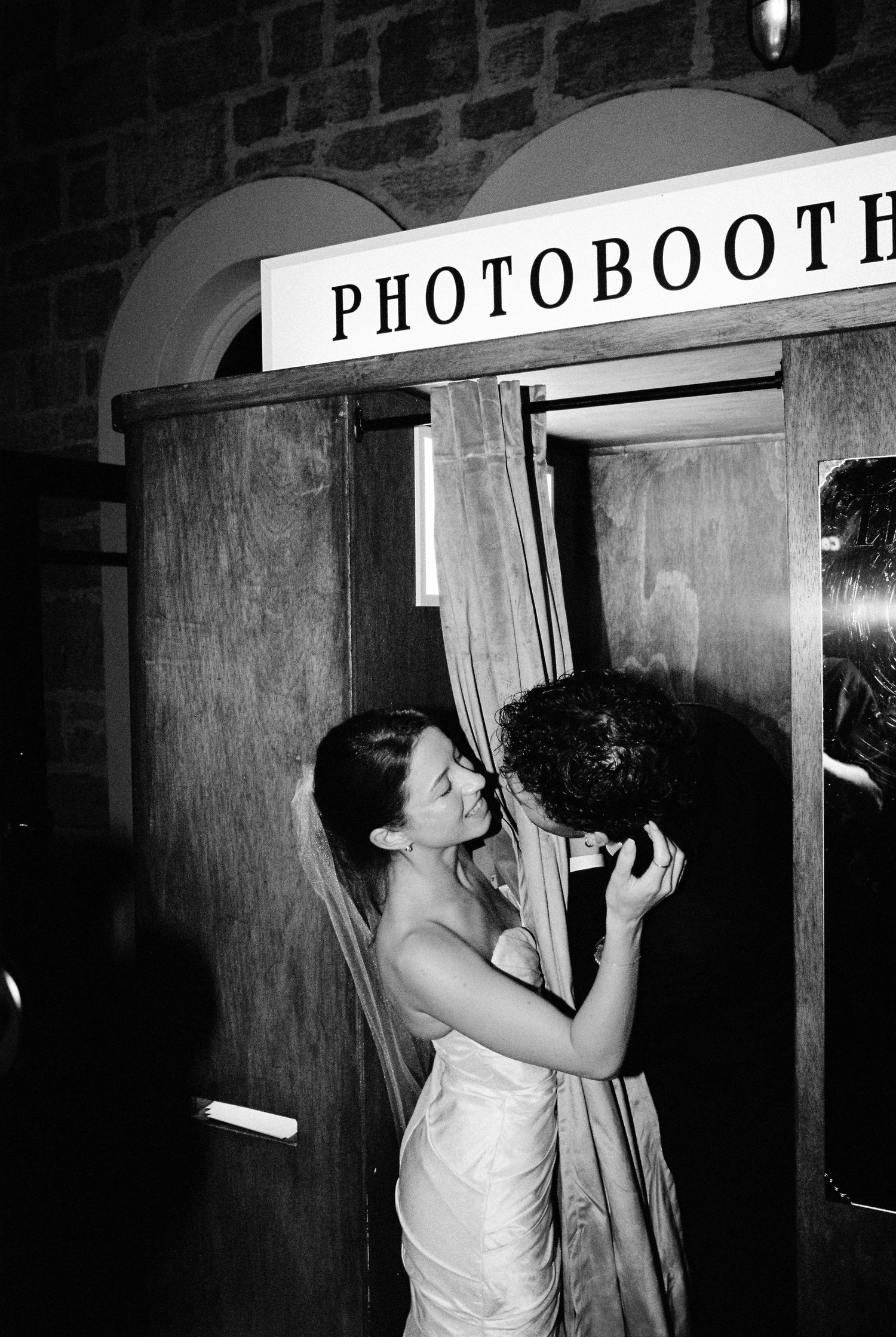 Bride and groom share a romantic kiss inside a vintage photobooth at their wedding reception.