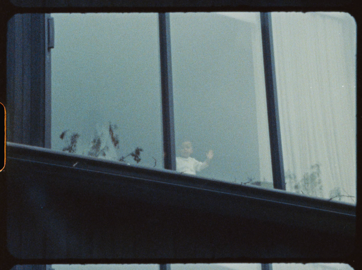 People waving through large glass windows viewed from outside building.