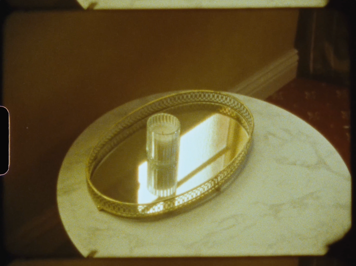Gold mirrored vanity tray with a crystal glass on a white marble side table in a warm-toned room.