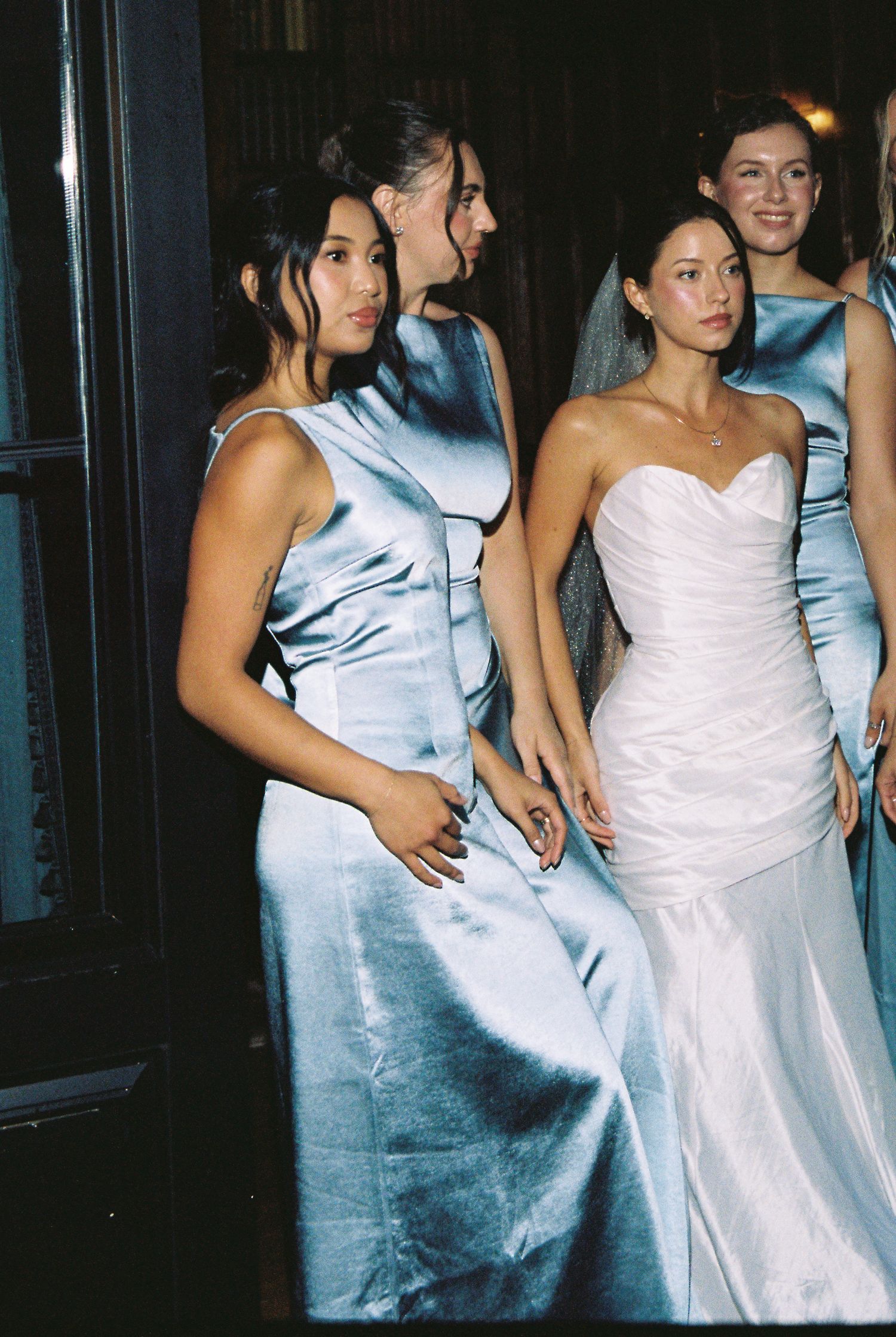 Bride in white gown with bridesmaids in blue satin dresses at elegant wedding reception.